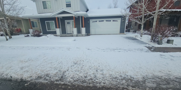 A two-story blue house with a white garage and porch covered in a light layer of snow on a cloudy winter day.