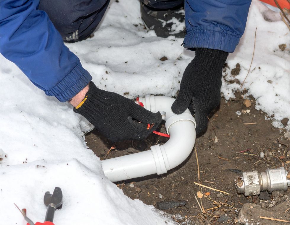 Person wearing black gloves connecting white PVC pipe in a snowy setting.
