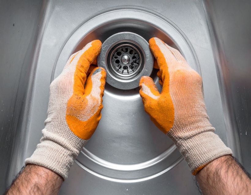 Gloved hands installing a metal sink drain