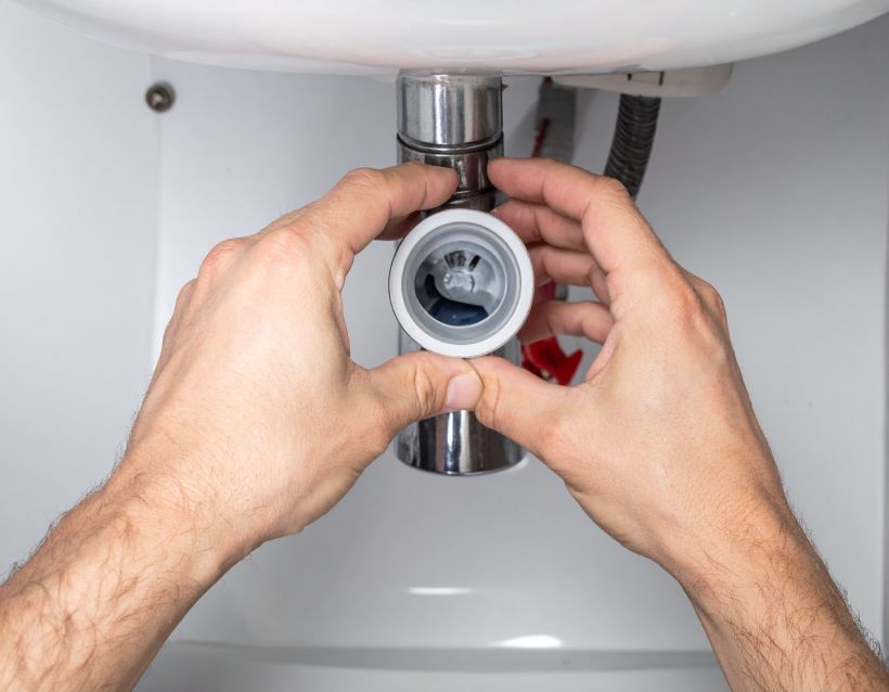 Hands installing a chrome sink drain pipe under a bathroom sink