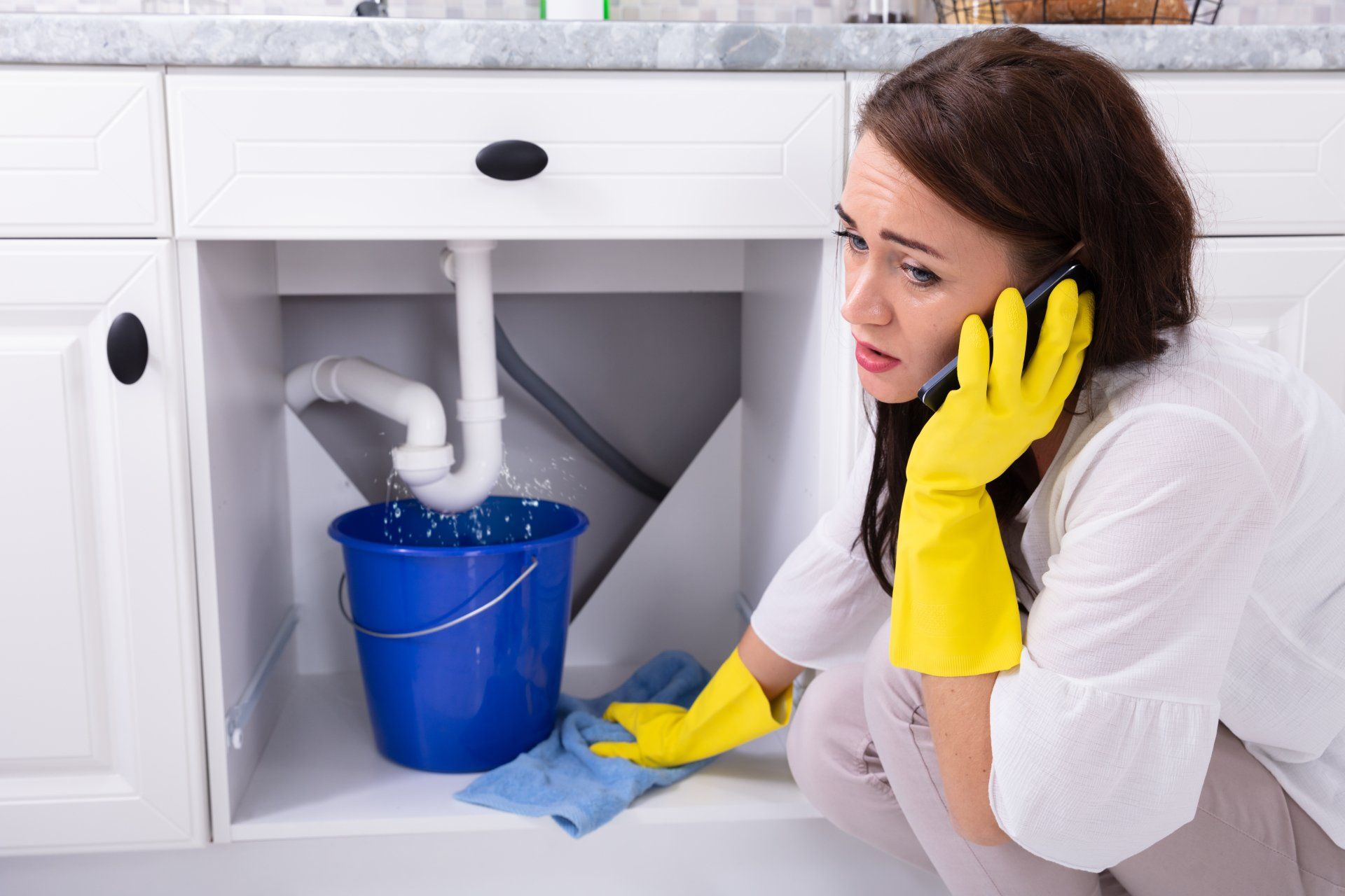 Woman with yellow gloves inspecting a leak under a sink — meridian plumbing