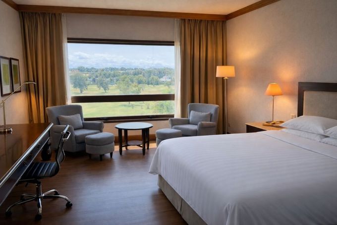 Habitación de hotel con cama king size, dos sillas junto a la ventana y un escritorio con vistas a un paisaje verde.