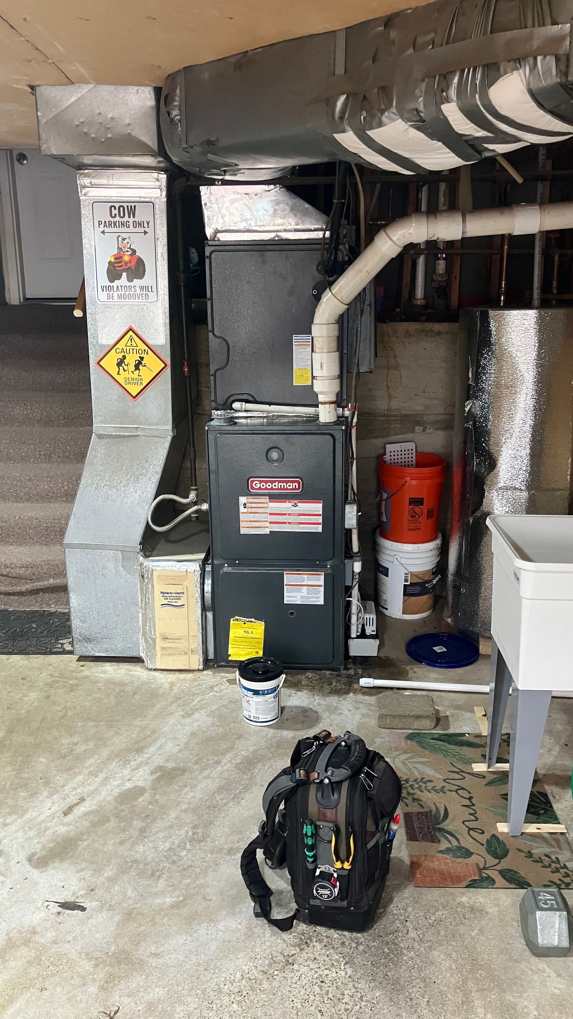 Furnace unit in a basement setting with ductwork, piping, and tools on the floor.