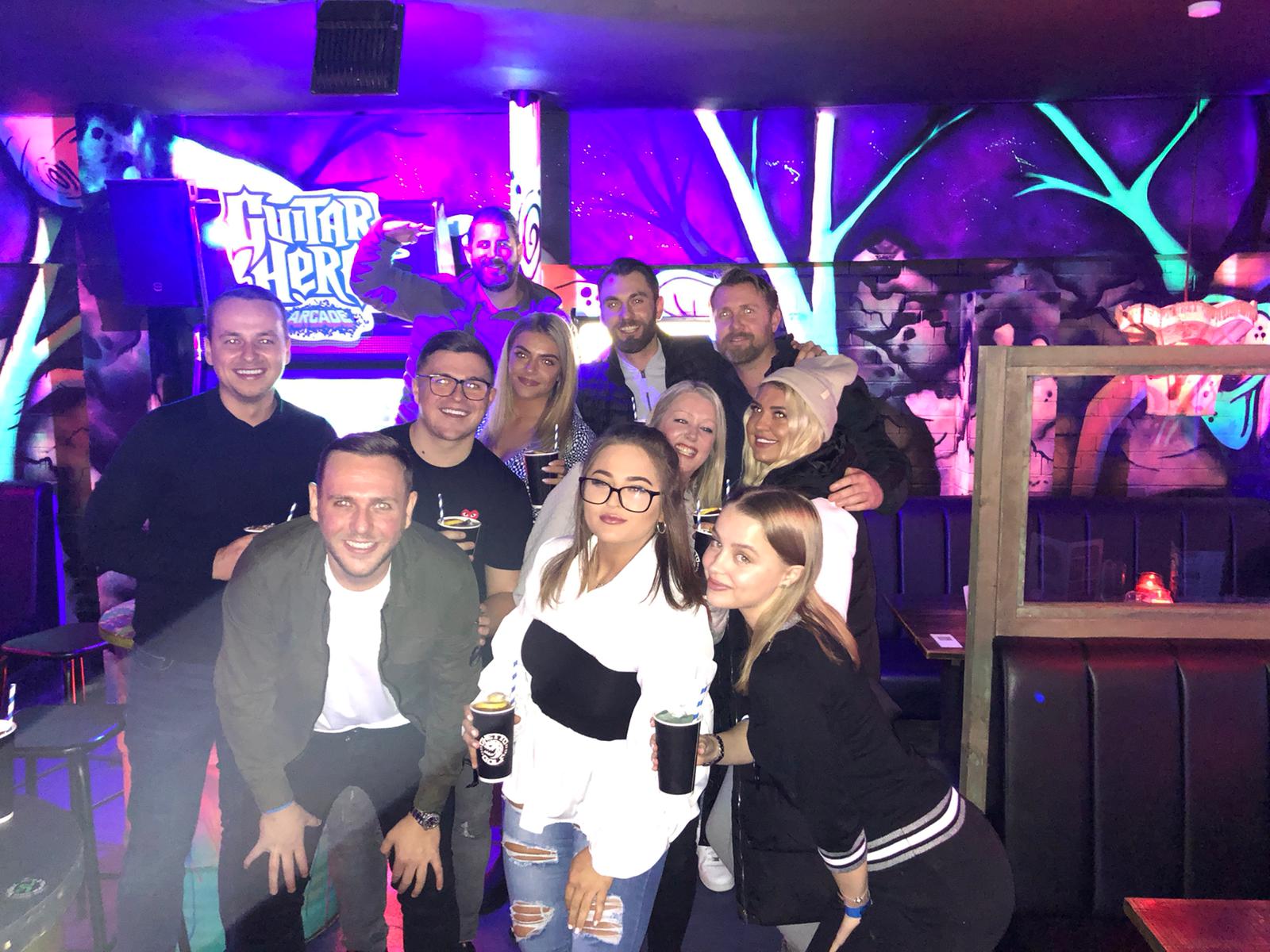 Group of people posing in a neon-lit nightclub with purple and blue lighting.