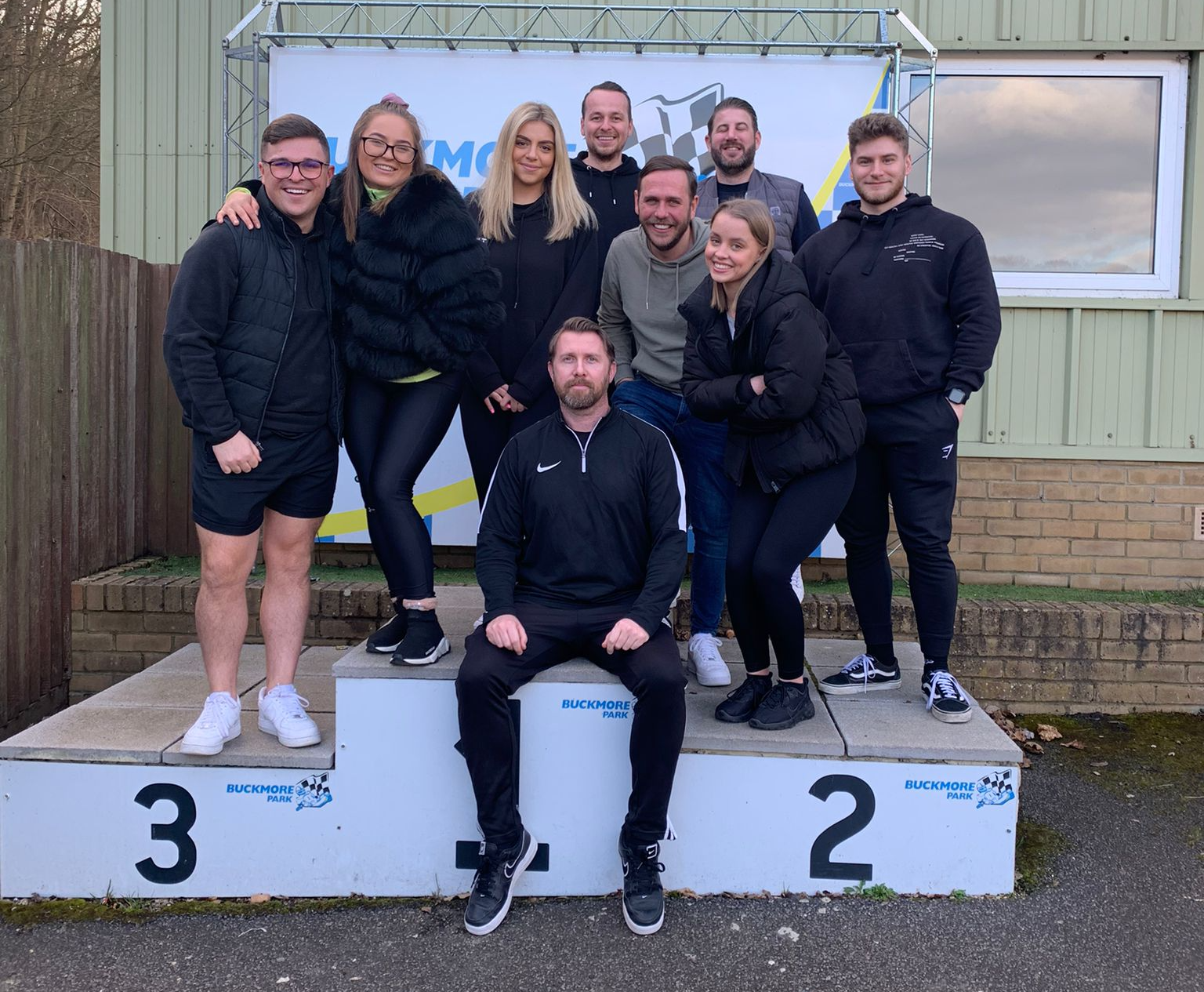 Group of people posing on a winners’ podium outdoors, smiling in dark jackets.