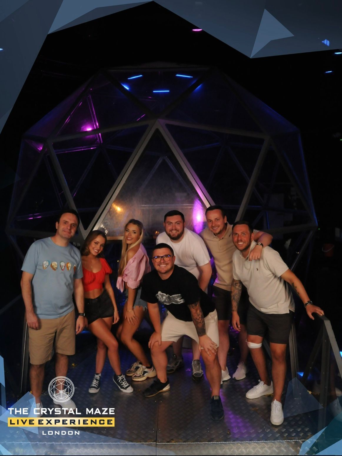 Group posing inside a glowing geometric maze, with neon purple and blue lights in the background.