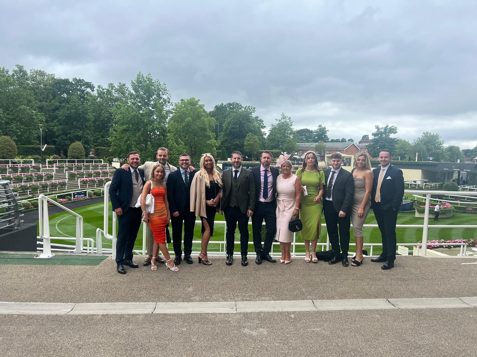 Group of people posing outdoors by a cemetery fence under a cloudy sky.