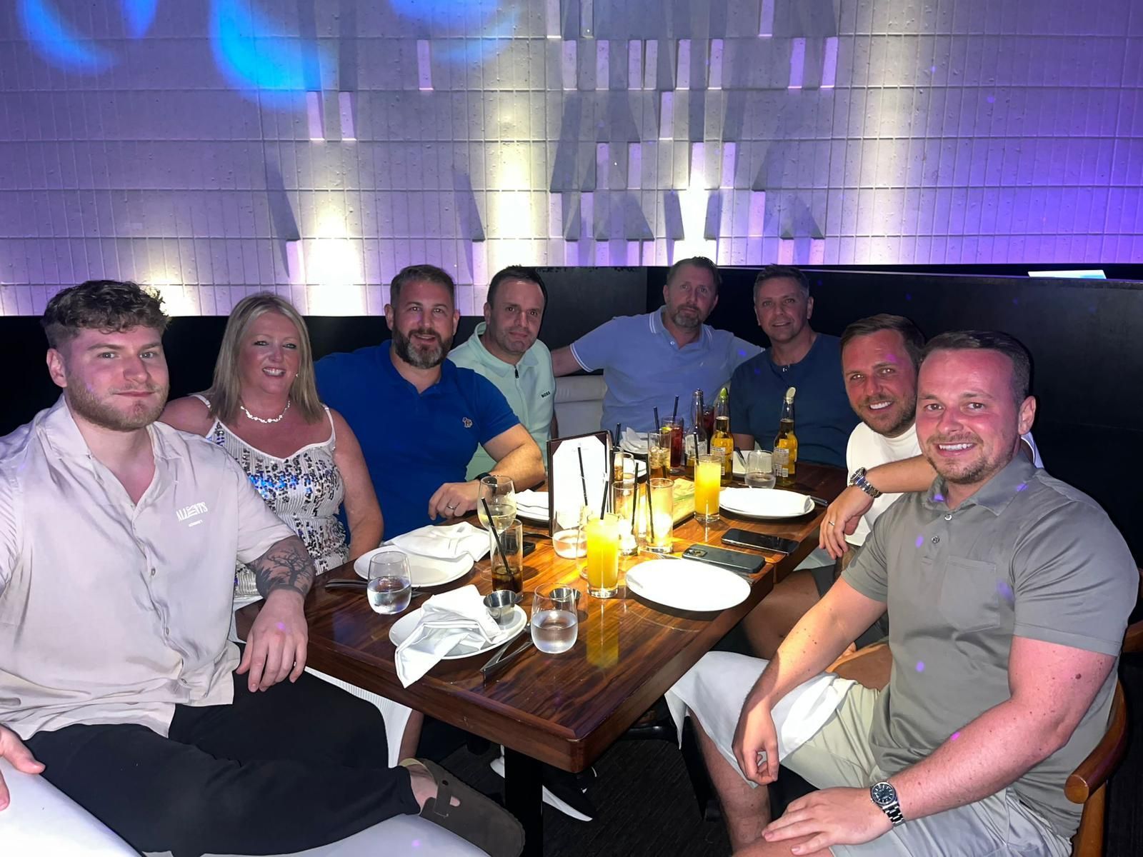 Group of people seated around a restaurant table, smiling under purple ambient lighting