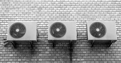 Three outdoor air conditioning units mounted on a brick wall.