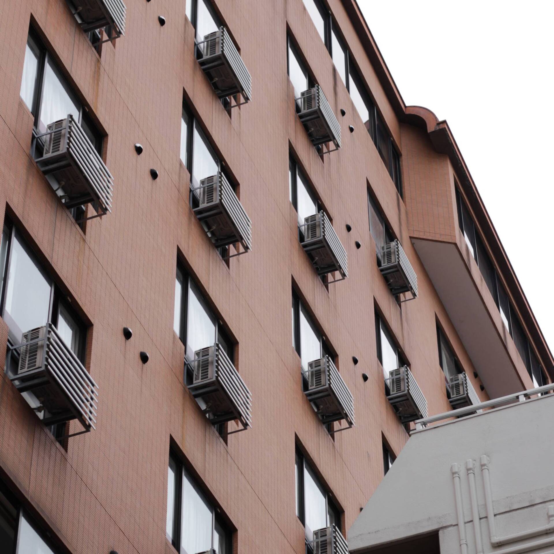 Pink apartment building with many windows and air conditioners, viewed from below against a gray sky