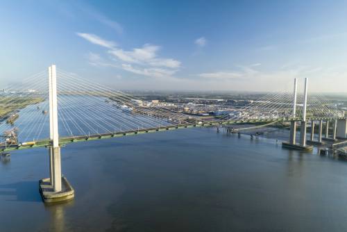 A cable-stayed bridge spanning a wide river under a clear blue sky with city buildings in the distance