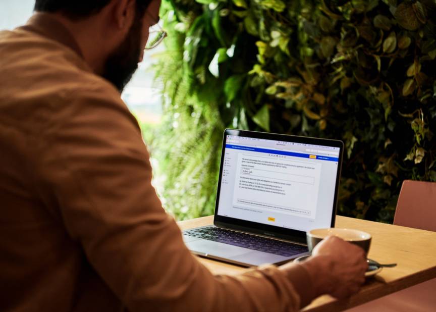 Person working on a laptop at a cafe table beside a wall of green plants
