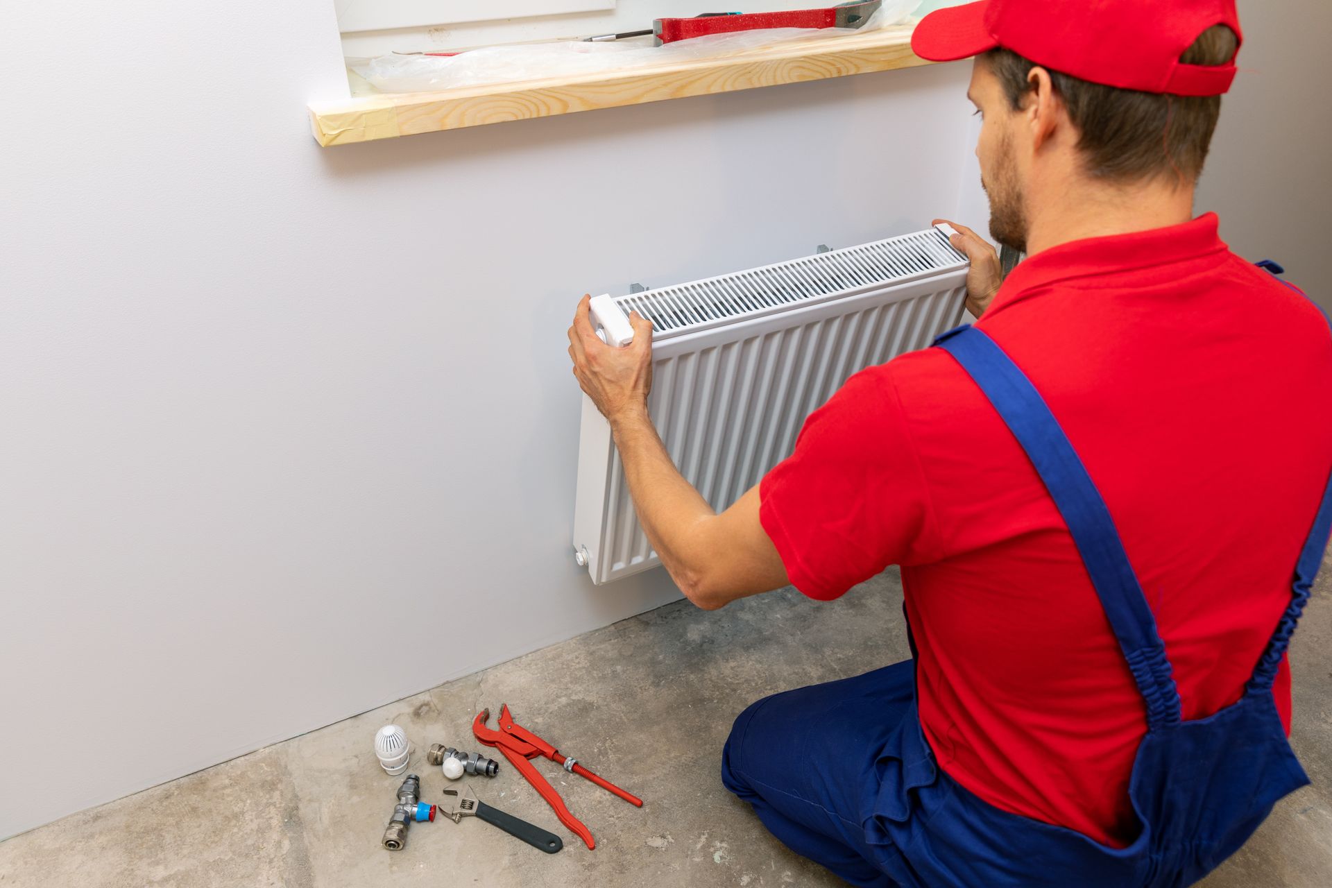 Plumber installing wall-mounted heating radiator with plumbing tools on floor. Plumber installing wall-mounted heating radiator with plumbing tools on floor.