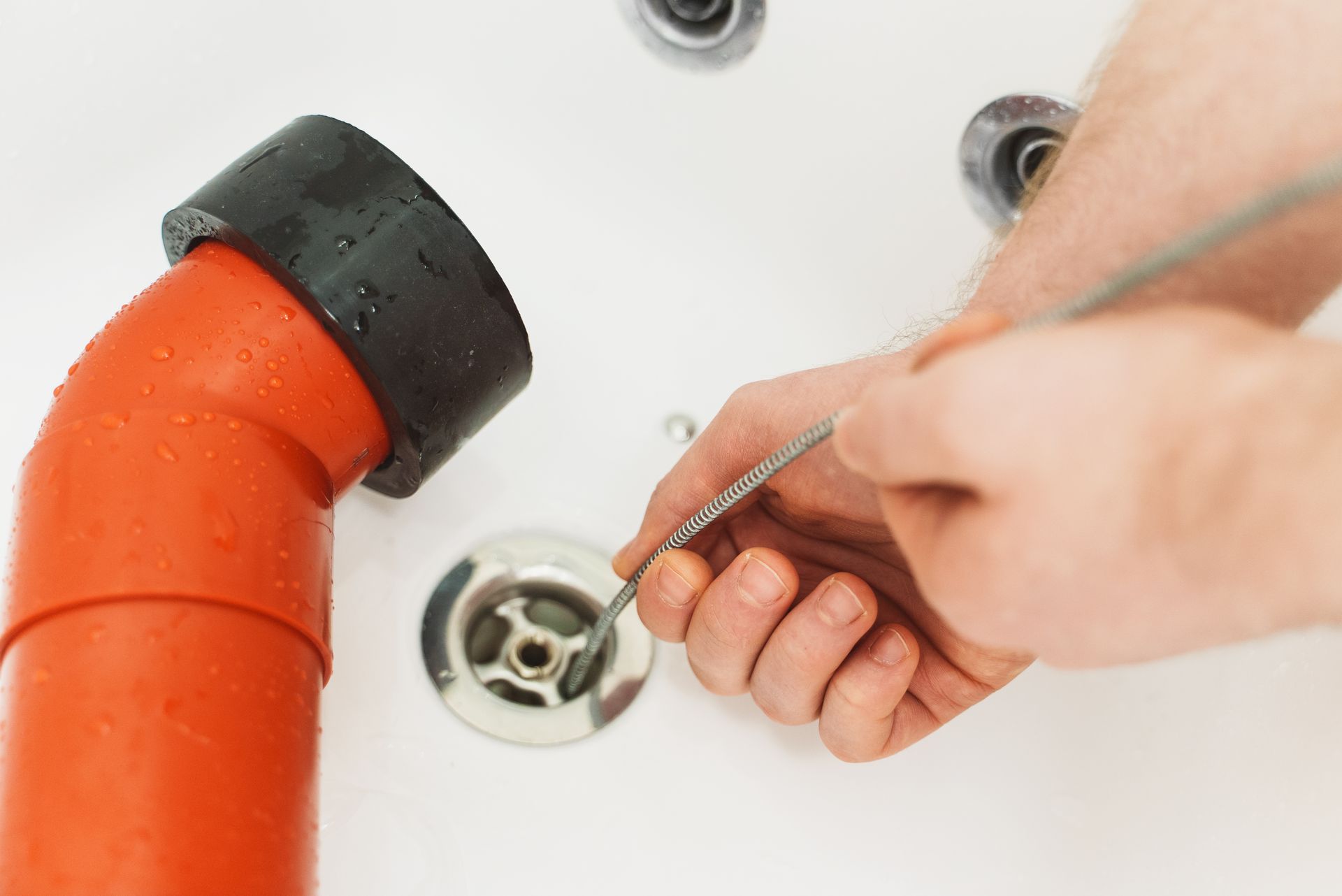 Close-up of a plumber using a drain snake to unclog a bathtub.