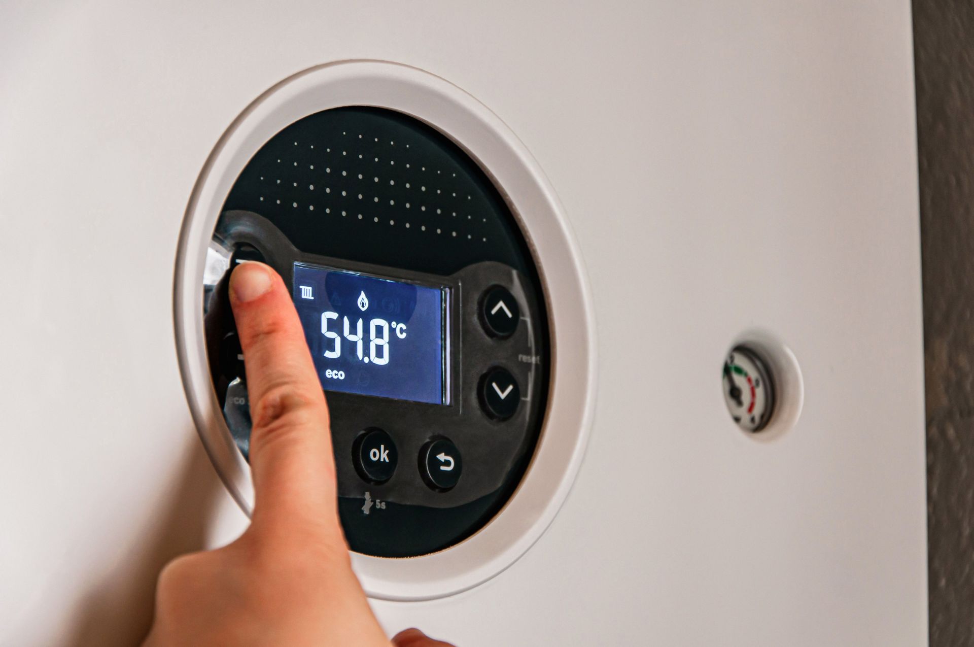 Hand adjusting a round thermostat display reading 54° on a white wall