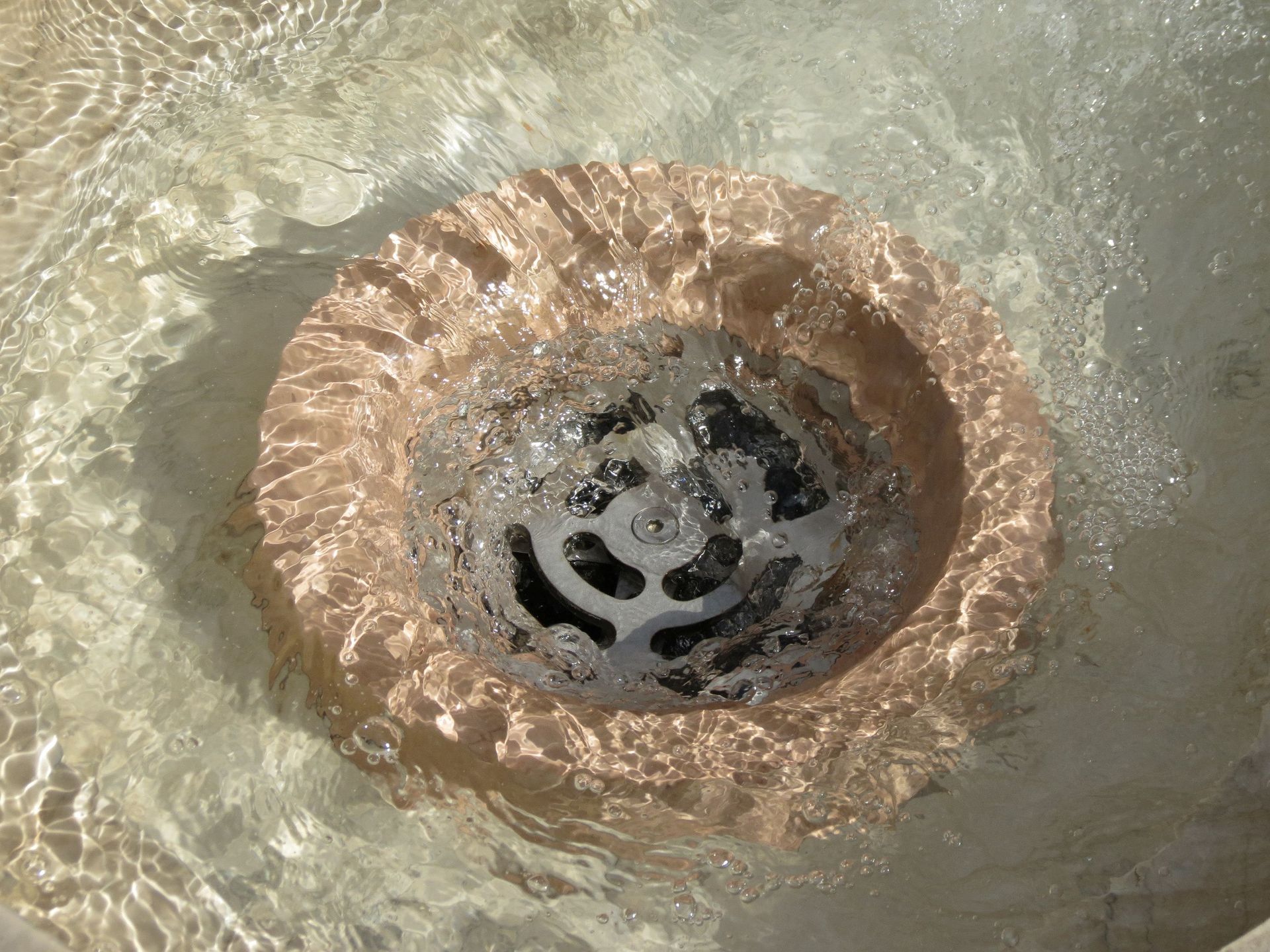 Close-up of a metal sink drain with water swirling around it