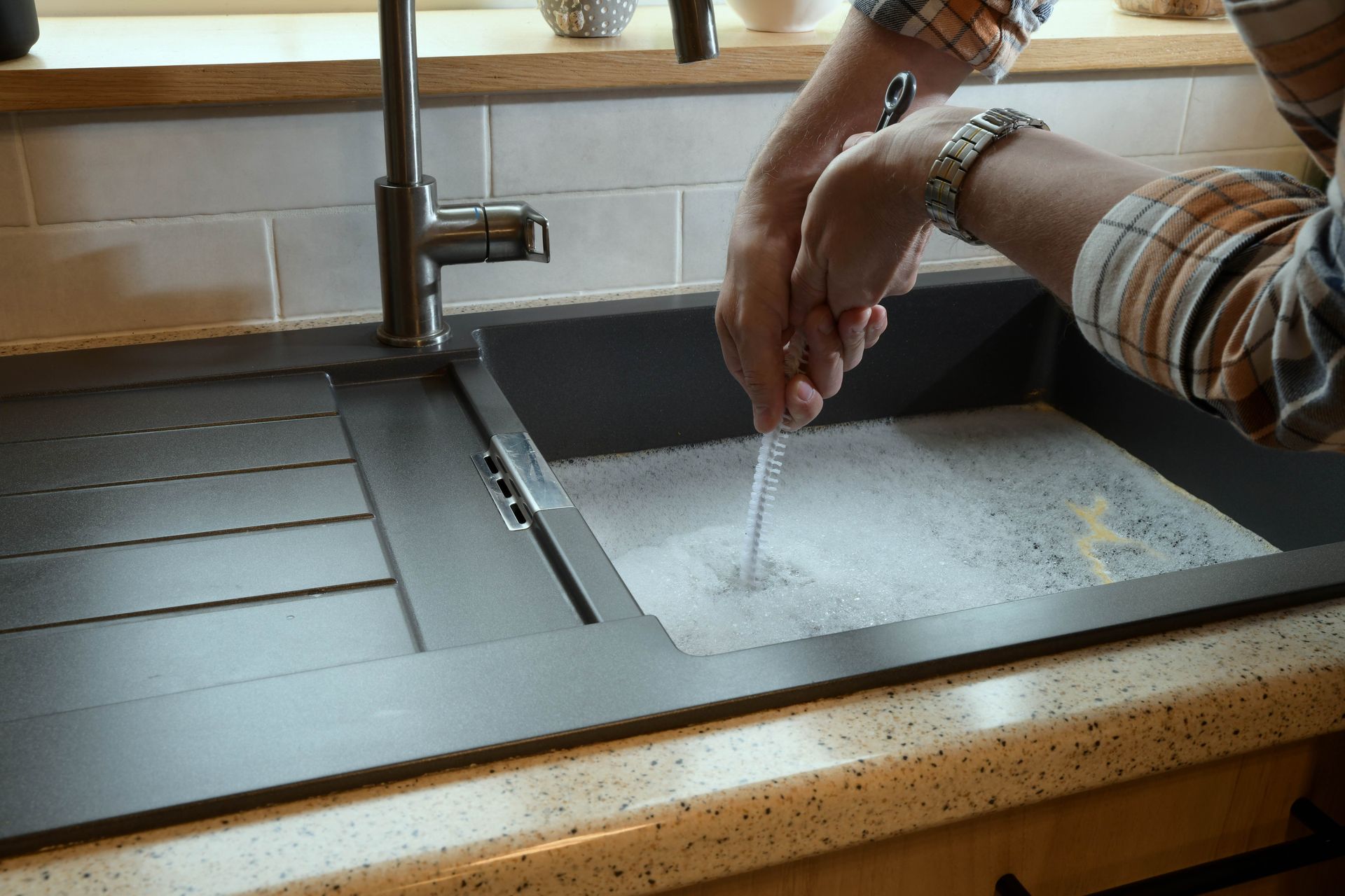 Hands rinsing under a kitchen faucet beside a sink full of soapy water