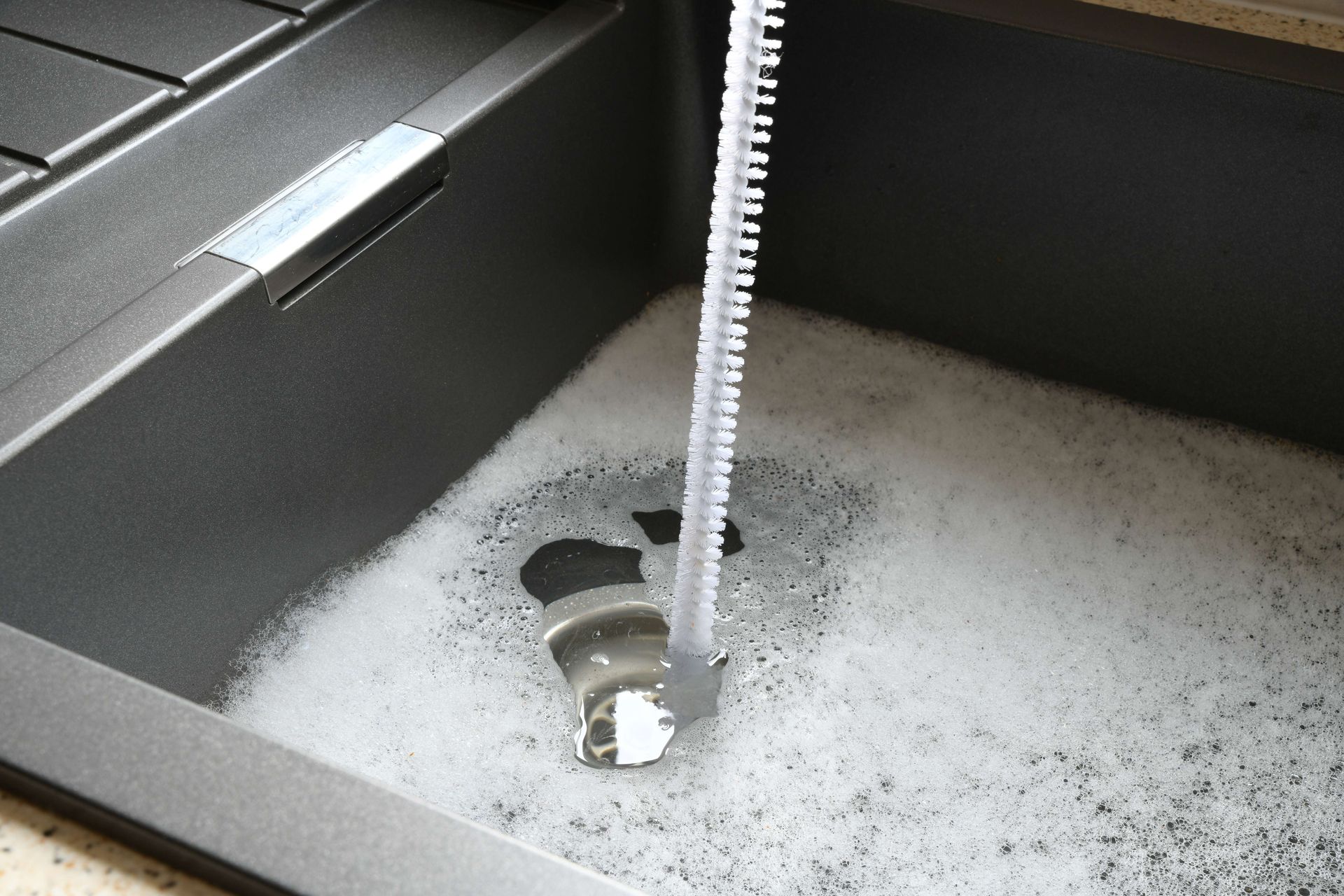 Sink with a spray of white foam and a brush scrubbing inside a gray basin