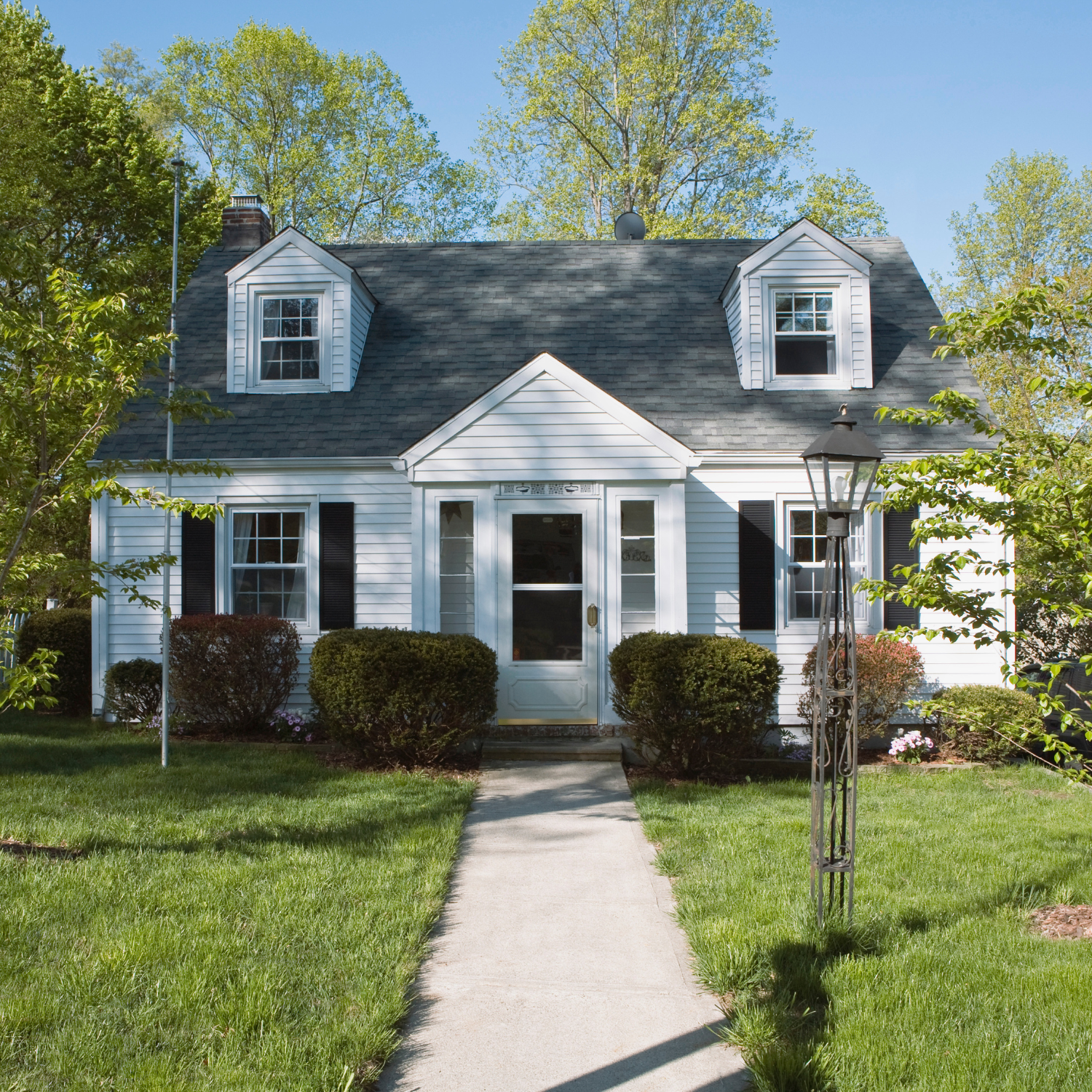 Small blue house with white trim, front walkway, dormer windows, and a grassy yard under trees