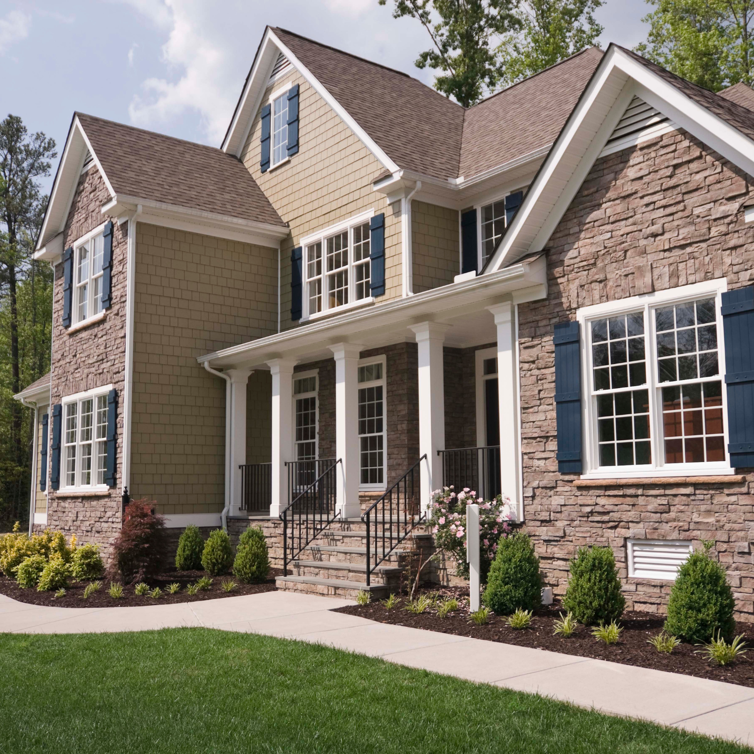 Two-story beige brick house with white trim, front porch, and landscaped lawn