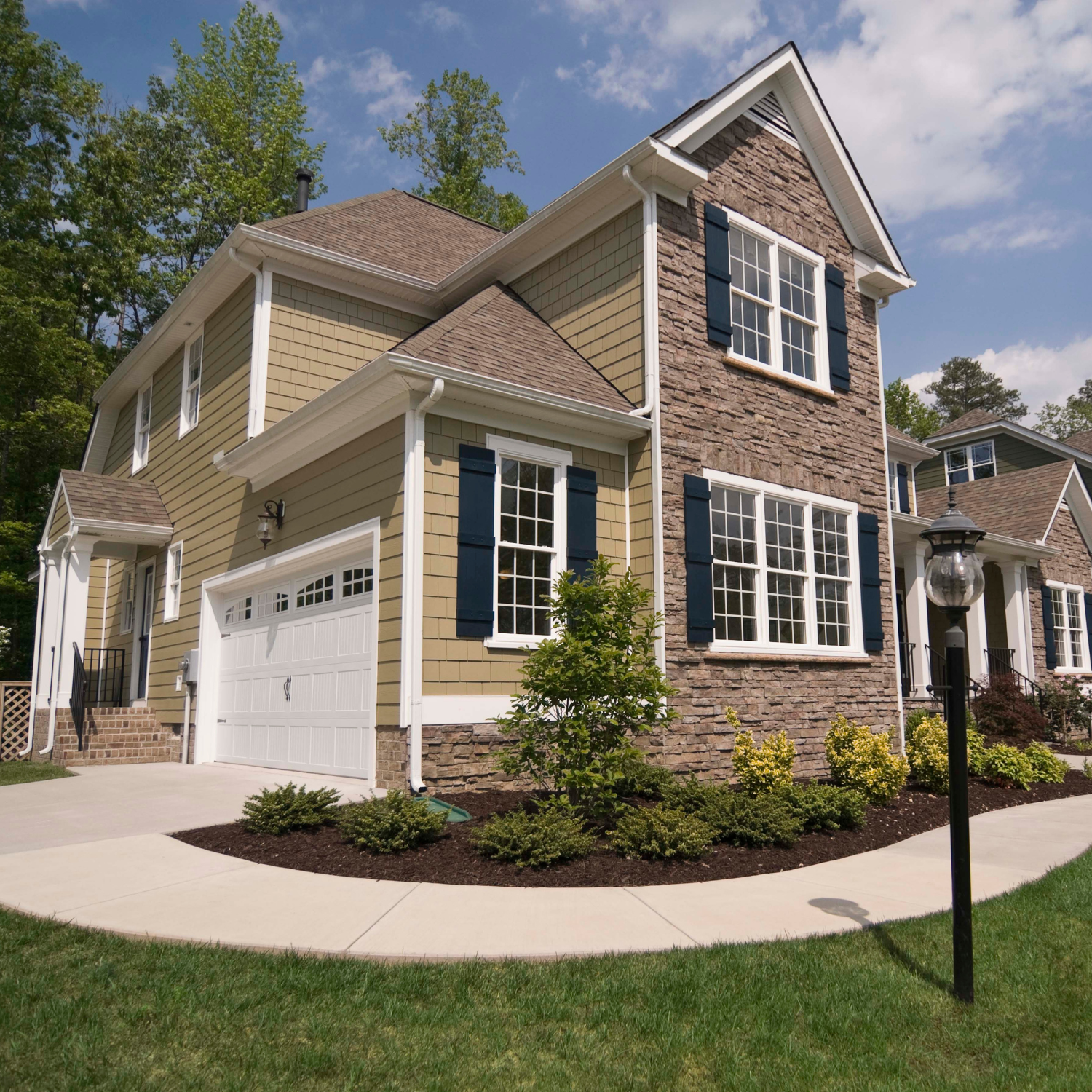 Two-story tan house with brick accents, white garage, and landscaped front lawn