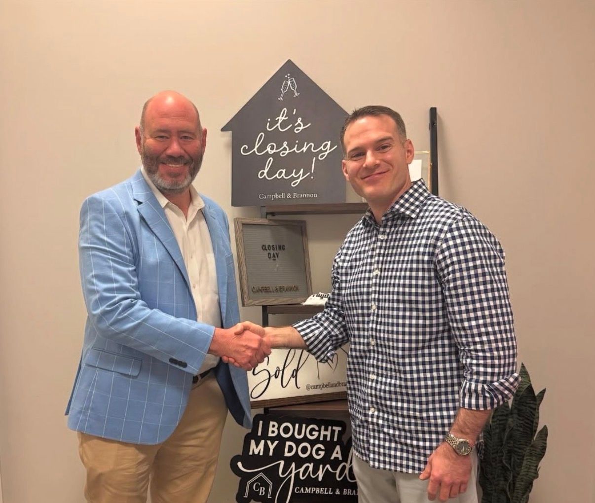 Two men shake hands beside a dog-themed sign in an indoor room.