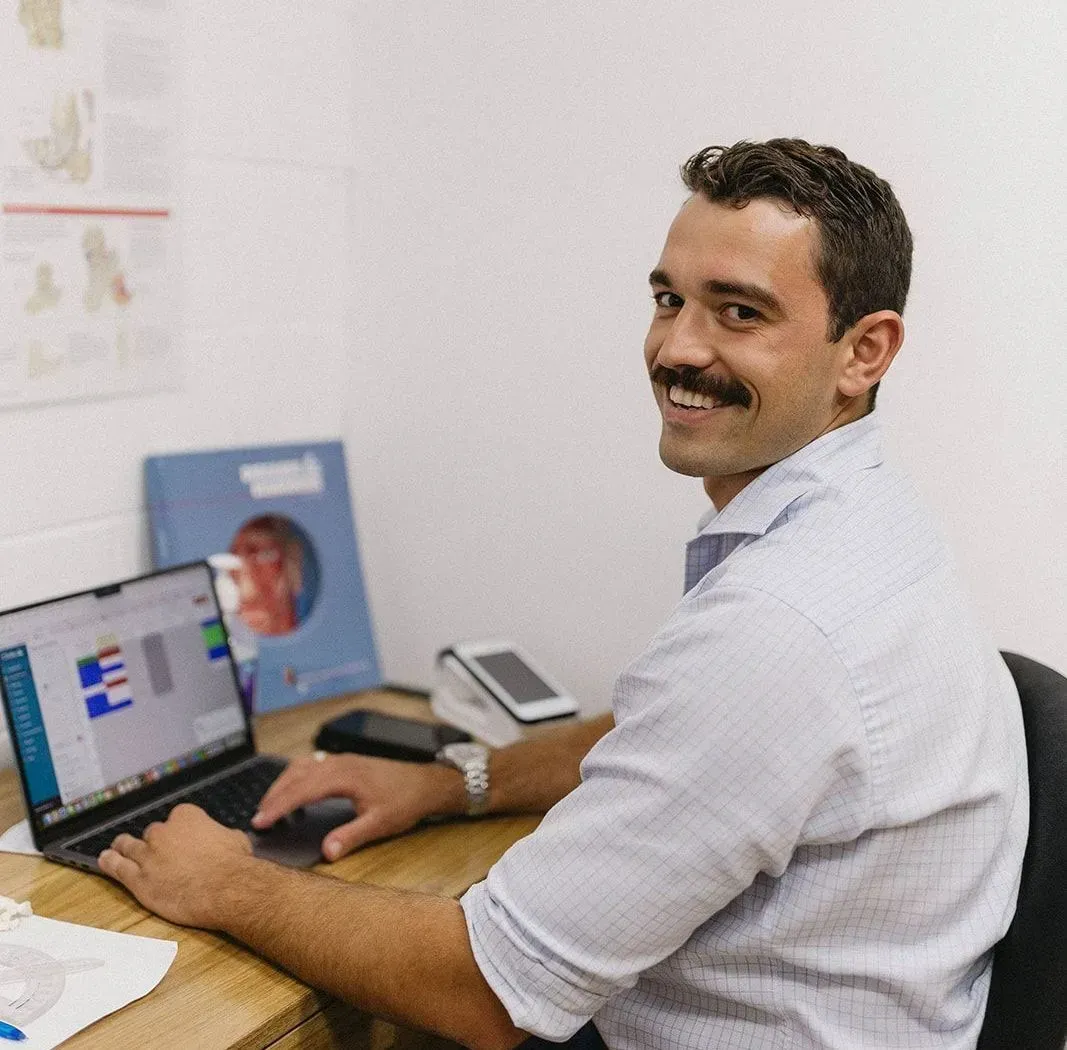 Man Smiling at A Desk with A Laptop, Typing in A Bright Office — Lord Street Podiatry in Port Macquarie, NSW