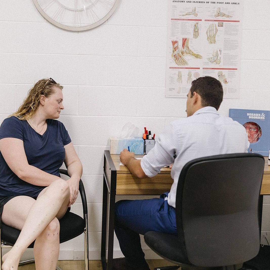 Two People Seated Across a Desk in a Clinic, Talking During an Appointment — Lord Street Podiatry in Port Macquarie, NSW
