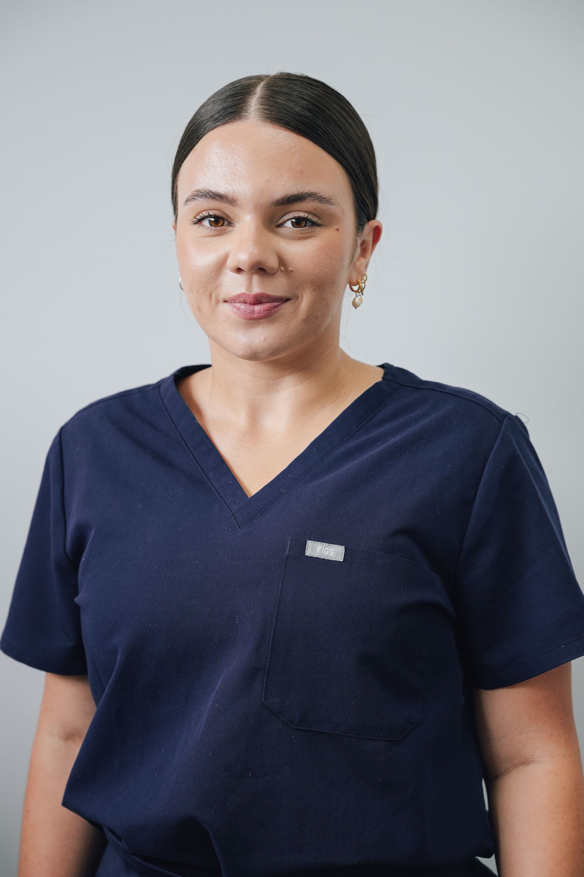 Person In Navy Scrubs Standing Against a Light Gray Background, Facing the Camera and Smiling Slightly — Lord Street Podiatry in Port Macquarie, NSW