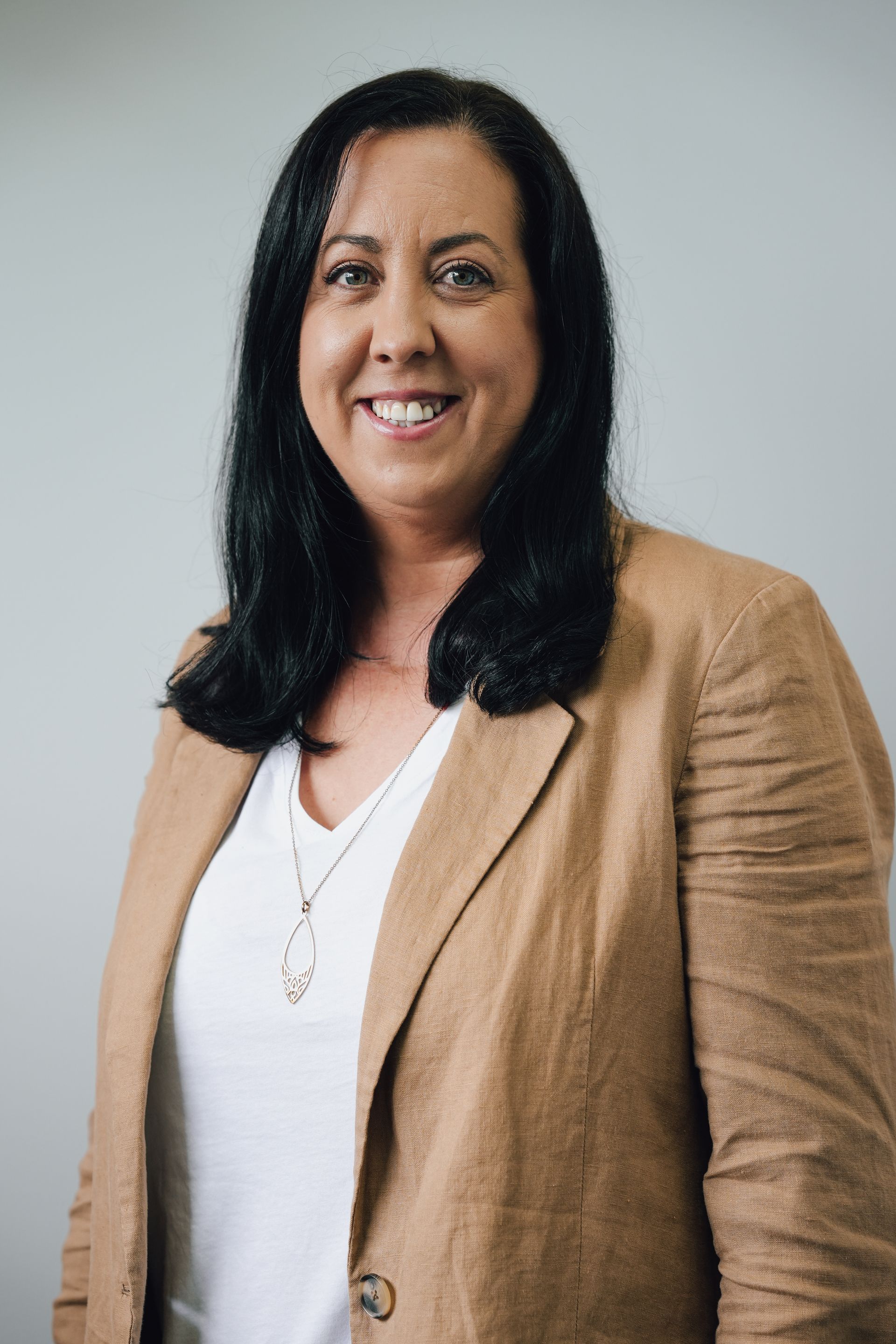 Smiling Woman in Tan Blazer and White Top Against a Light Gray Background — Lord Street Podiatry in Port Macquarie, NSW