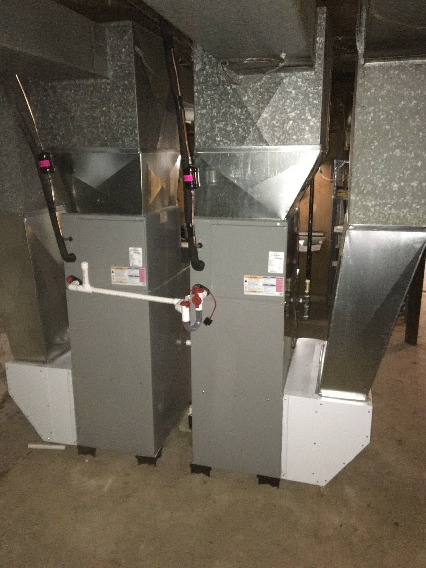 Two gray HVAC units with ductwork in a utility room.
