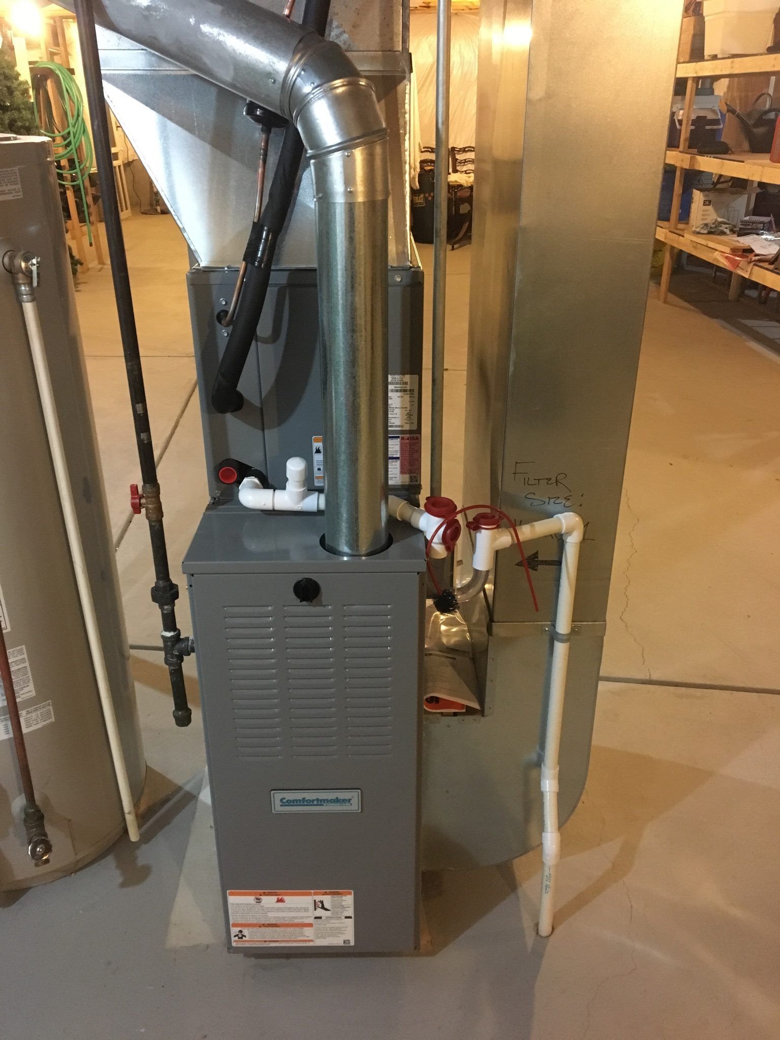 Furnace with metal vent pipes and white plastic piping in a basement.