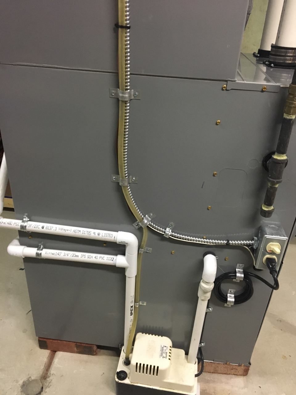 Gray HVAC unit with connected pipes, electrical wiring, and a condensate pump.