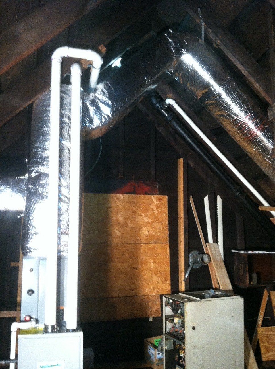 Furnace and ductwork in an attic, featuring silver insulated pipes and wooden structures.
