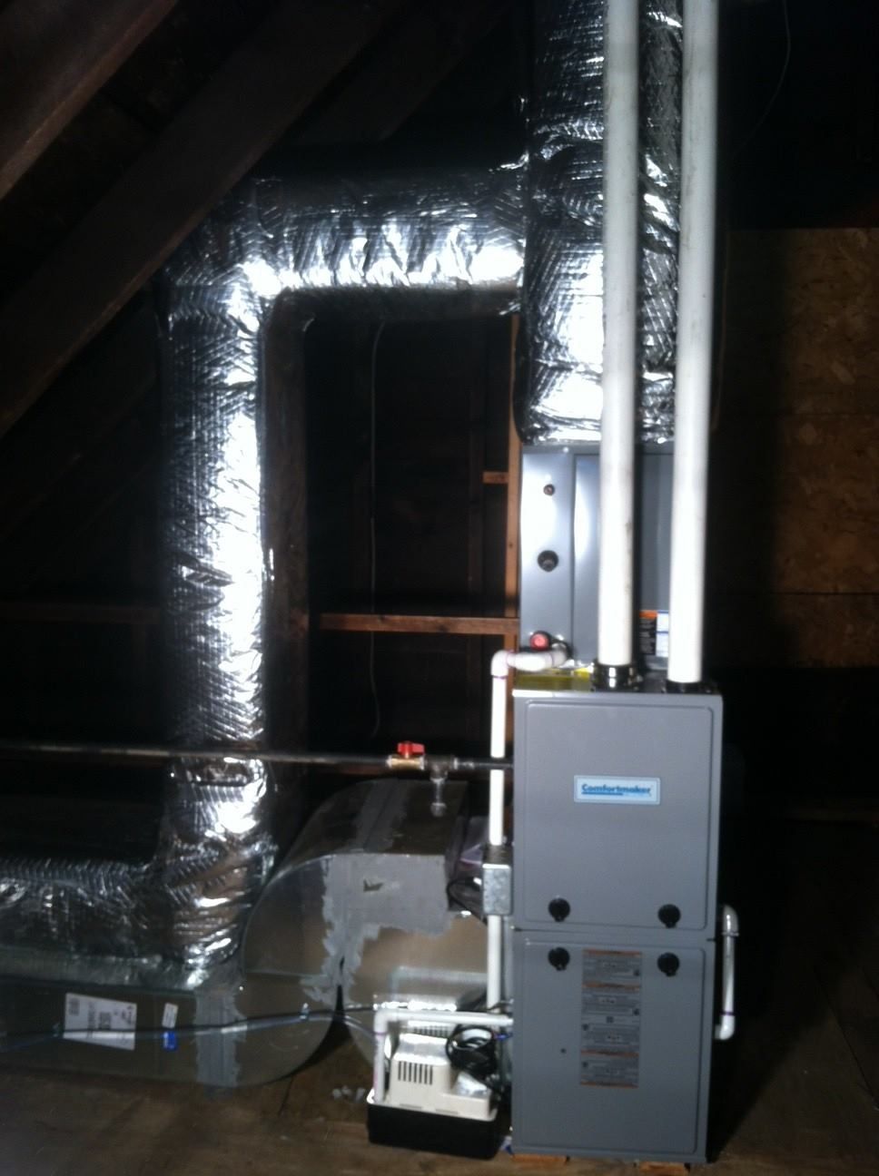 Furnace and ductwork in an attic, with metallic insulation and PVC pipes.