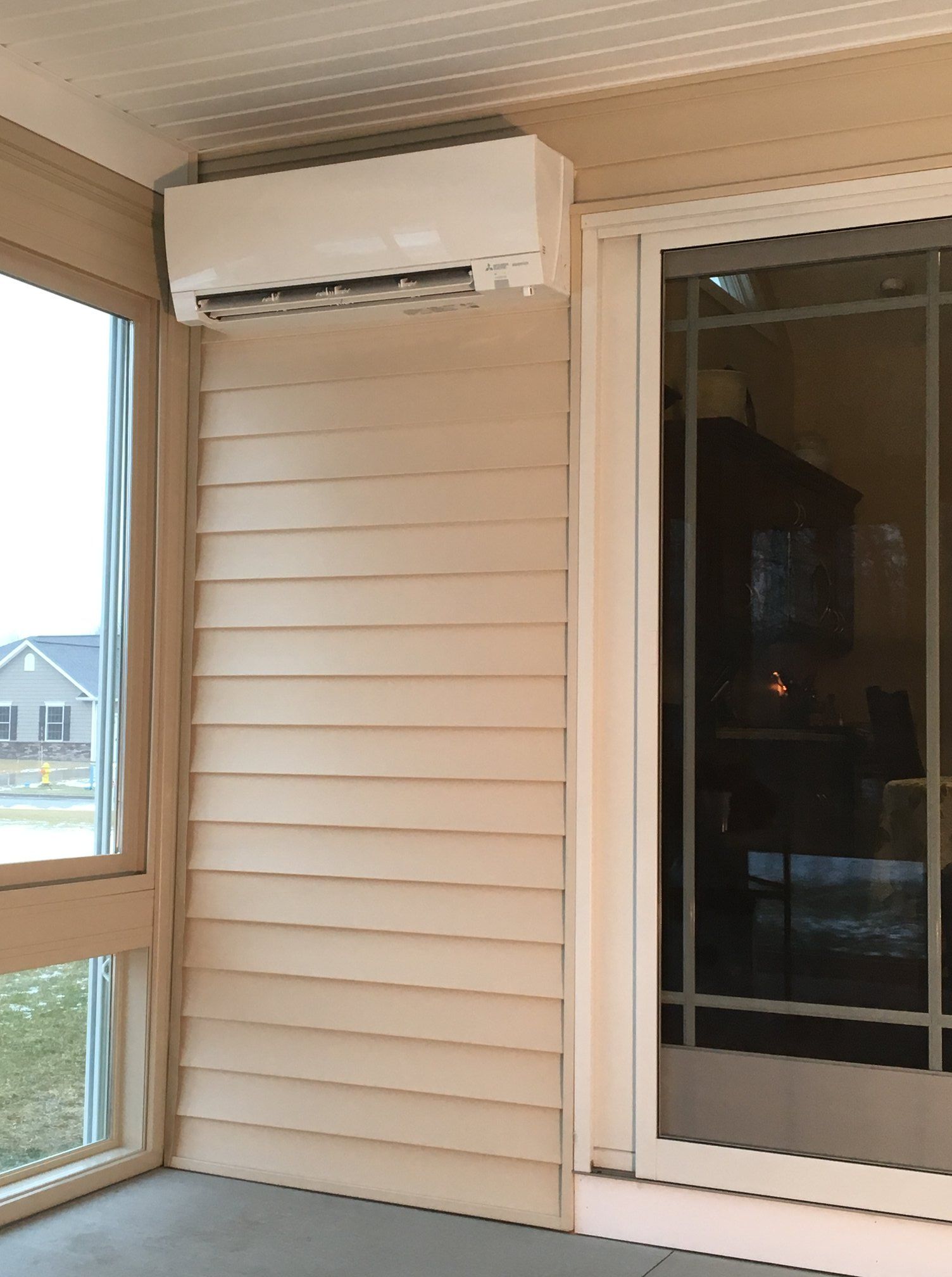 White air conditioning unit mounted on a light beige wall next to a glass sliding door.