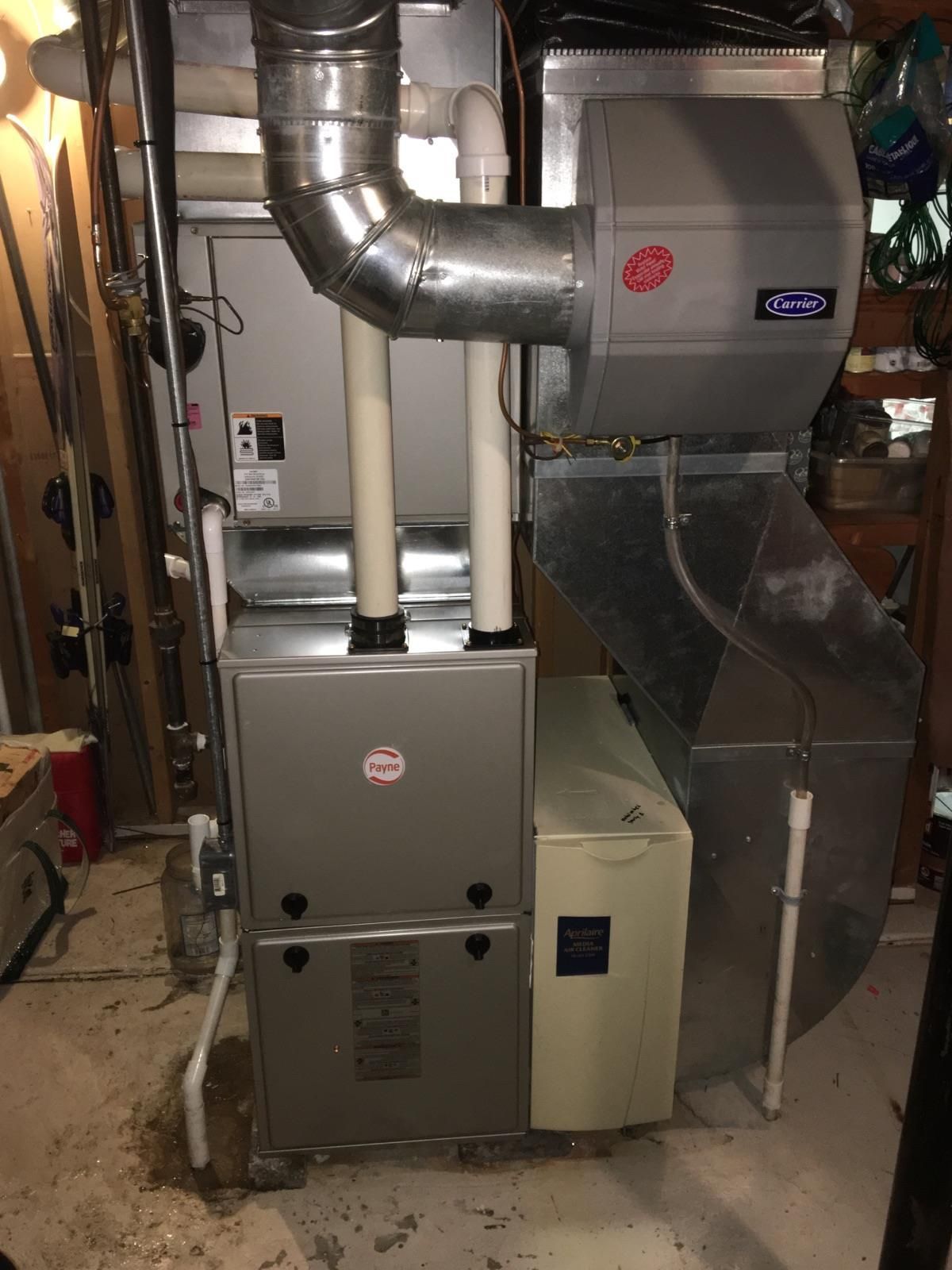 A gas furnace and humidifier in a basement setting. Silver metal unit with ductwork and piping.