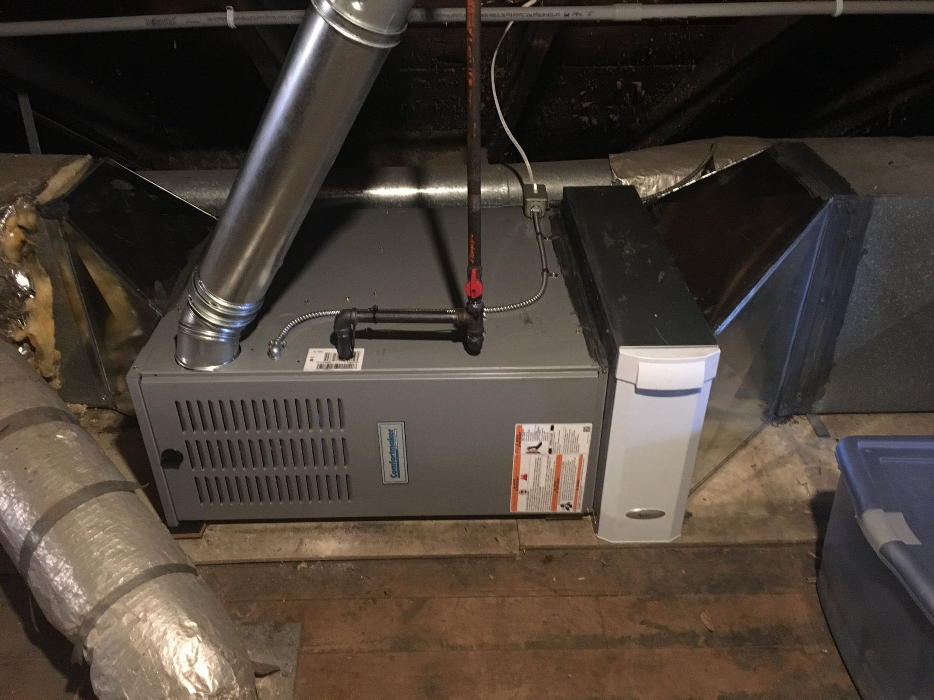 A gas furnace in a dark attic with ductwork, vent pipe, and a humidifier attached.