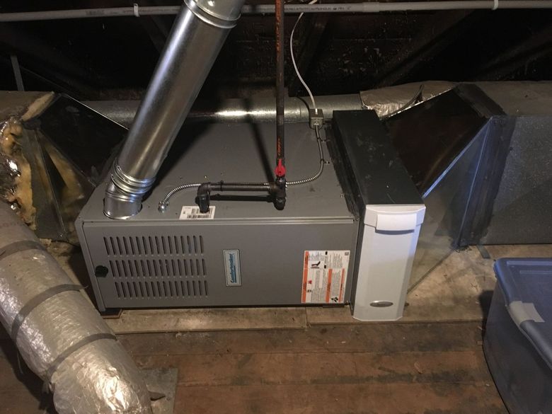A gas furnace in a dark attic with ductwork, vent pipe, and a humidifier attached.