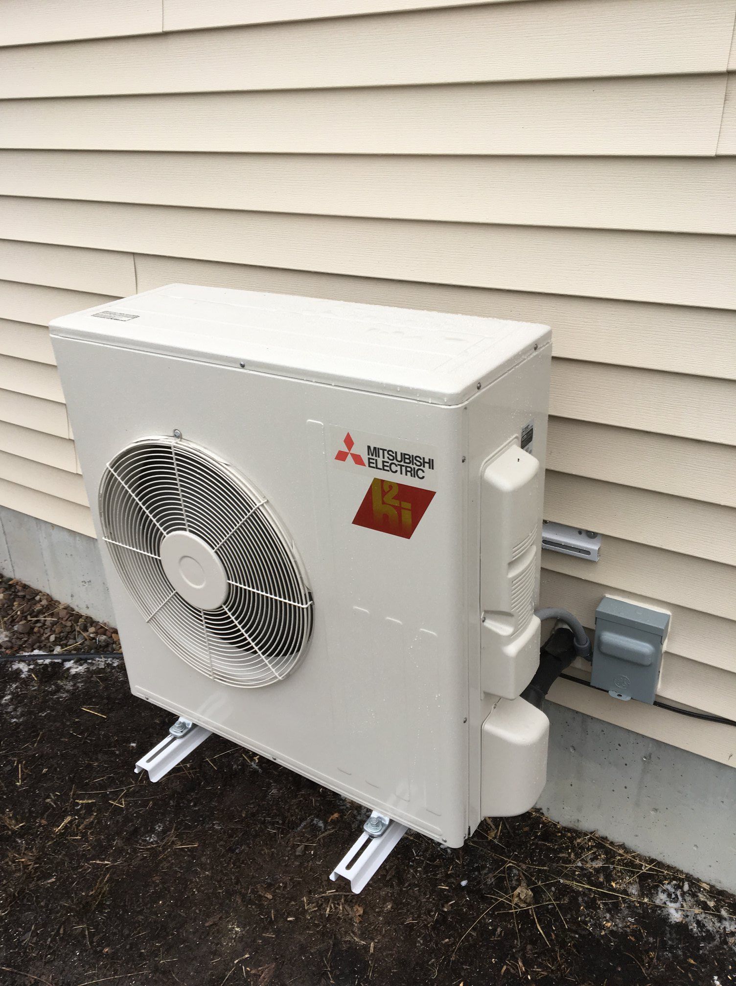 White Mitsubishi outdoor heat pump unit mounted on a light-colored building's exterior.