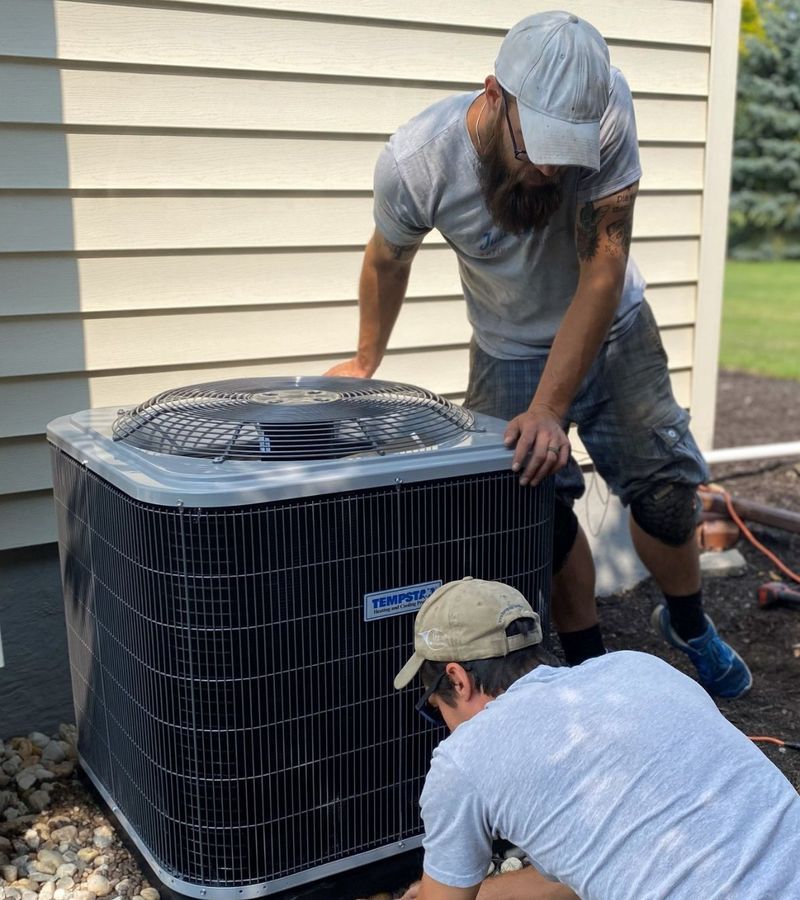 Two workers installing an air conditioning unit near a house.