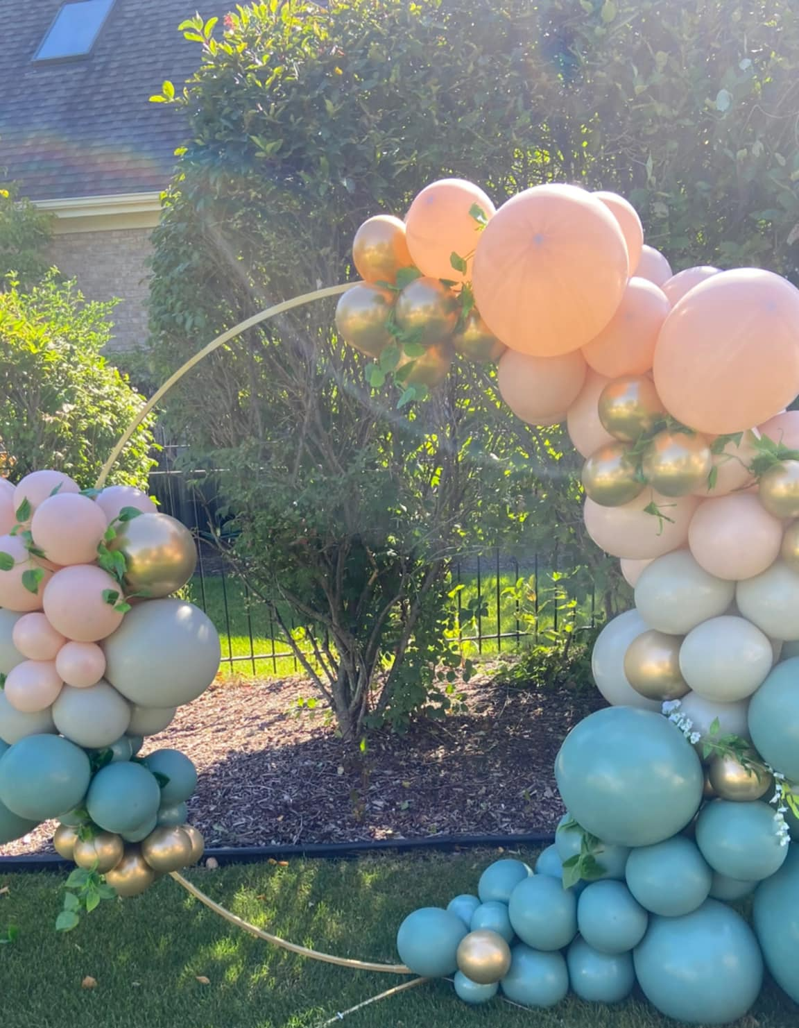 Outdoor baby celebration decor in Hobart, IN, featuring a gold ring with a dusty blue, pale pink, and gold-accented balloon garland, perfect for a photo op.