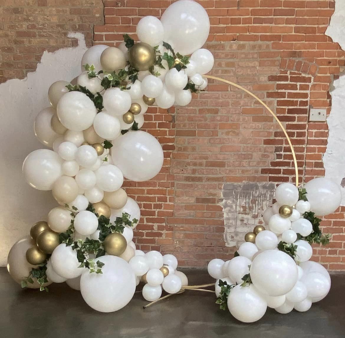 Gold circle arch adorned with neutral balloon colors, gold and beige accents, and ivy vines for a pop of color, creating a boho-inspired, elegant, and organic photo backdrop at Ember's in Rensselaer, Indiana. Perfect for a wedding celebration.