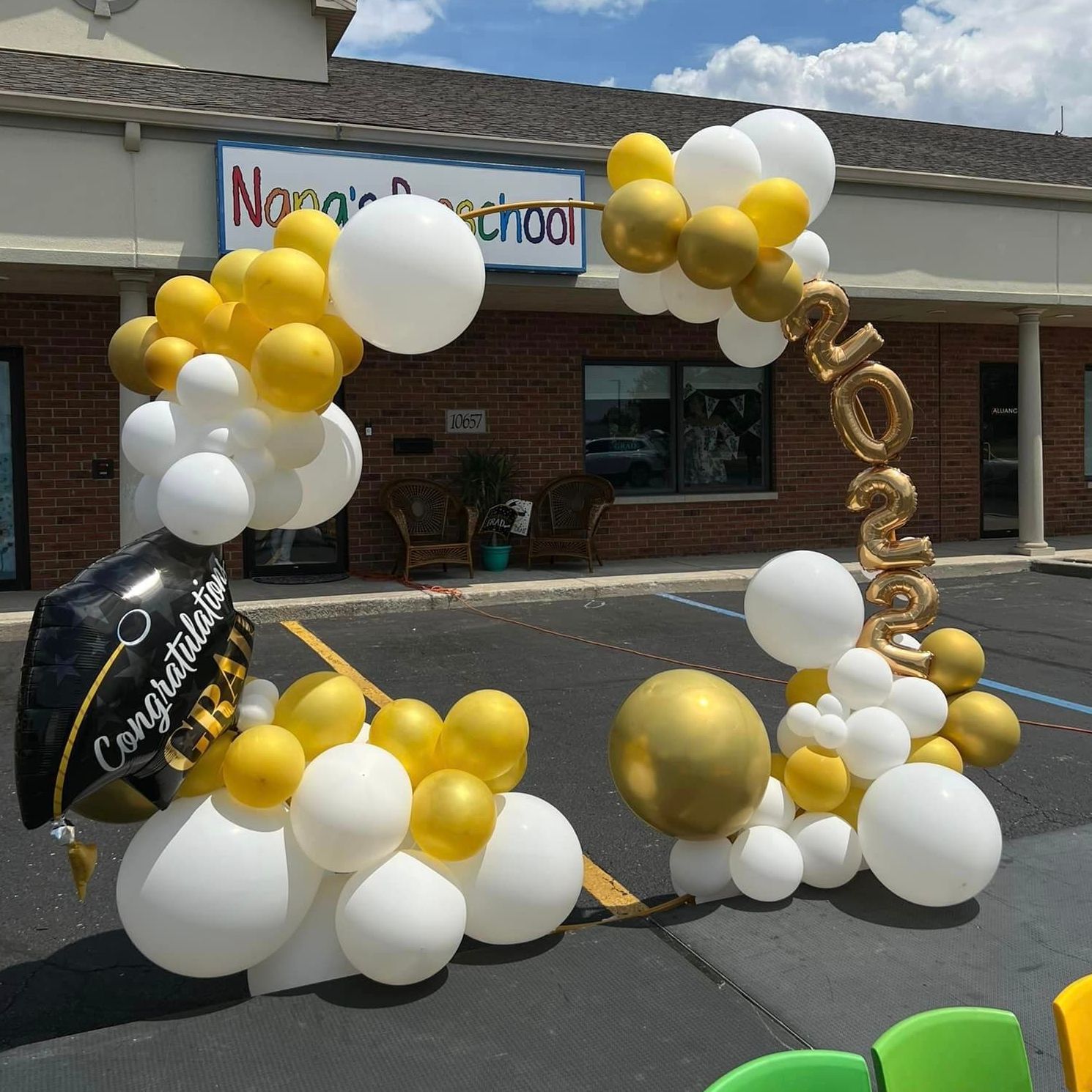 Preschool graduation celebration at Nana's Preschool in Winfield, Indiana, featuring a split gold hoop with organic party poof balloons in yellow and white with gold accents. Decor includes foil graduation year balloons and a foil graduation cap, creating a festive and cheerful 'Congratulations Grad' display.