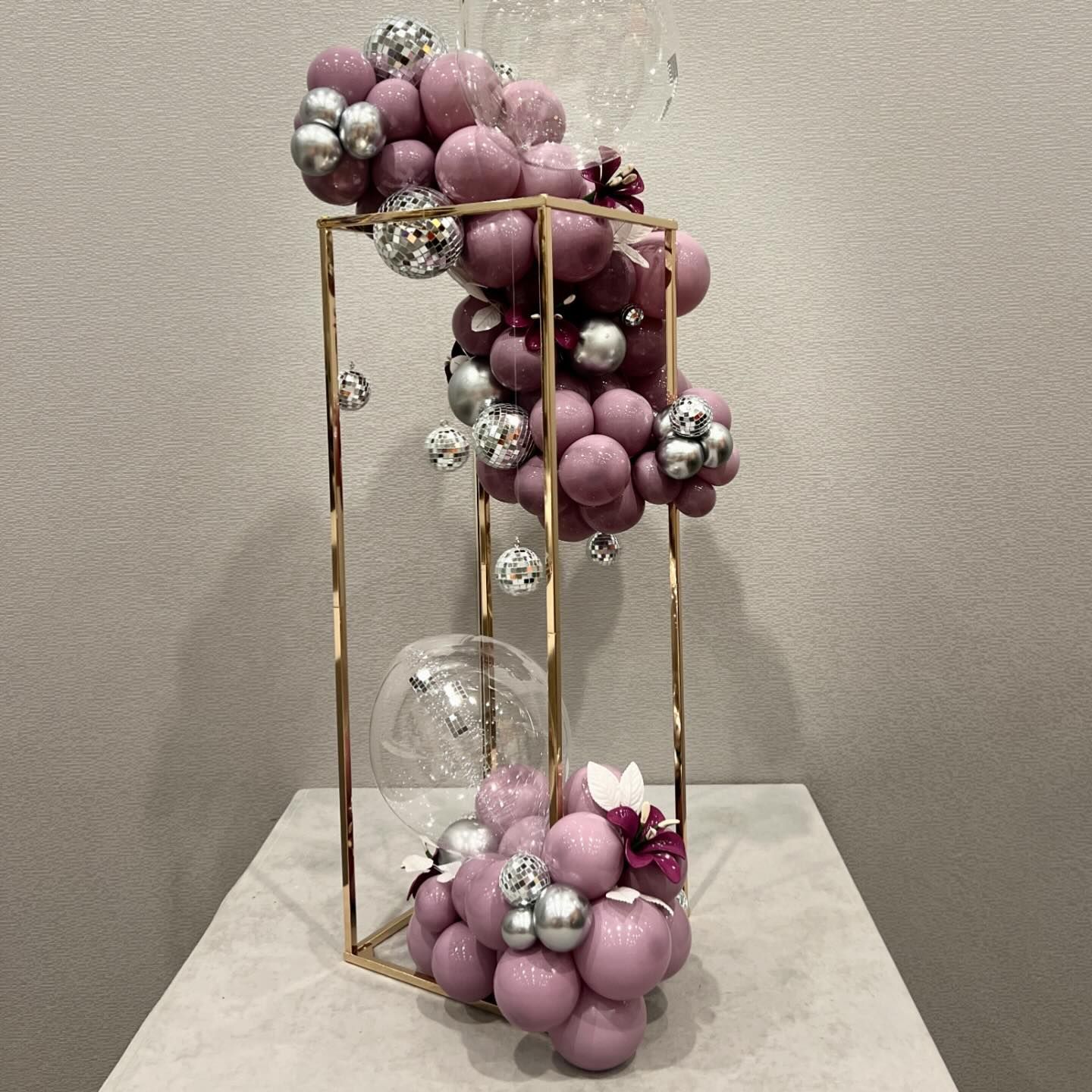 Wedding reception centerpiece featuring a 3D gold rectangle with a luxury balloon garland weaving throughout. The garland showcases dusty lilac, sangria purple, chrome silver, and clear balloons, accented with disco balls for a jaw-dropping, organic design. Award-winning decor in Chicago, IL, perfect for making a statement at your celebration.