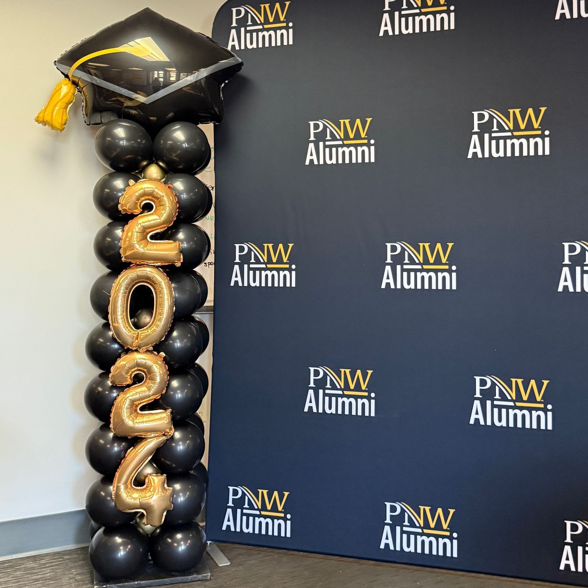 Purdue University commencement ceremony featuring a square-packed balloon column with foil numbers and a grad hat topper, placed next to a step-and-repeat backdrop. A sleek and clean photo opportunity with a classic style.