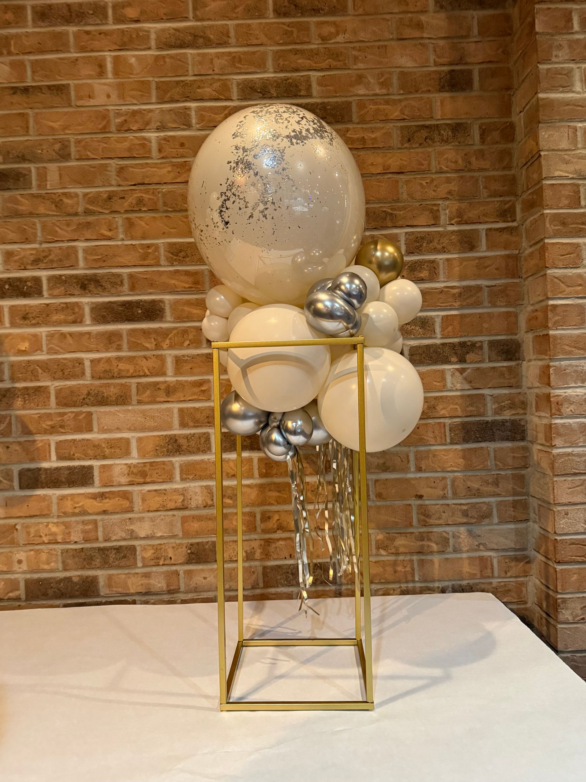 Deluxe and elegant gold centerpiece featuring a silver confetti balloon topper, complemented by neutral and chrome-colored balloons perfectly shaped to match your event's theme. Accented with a fun shimmer curtain for a customized and dazzling touch.