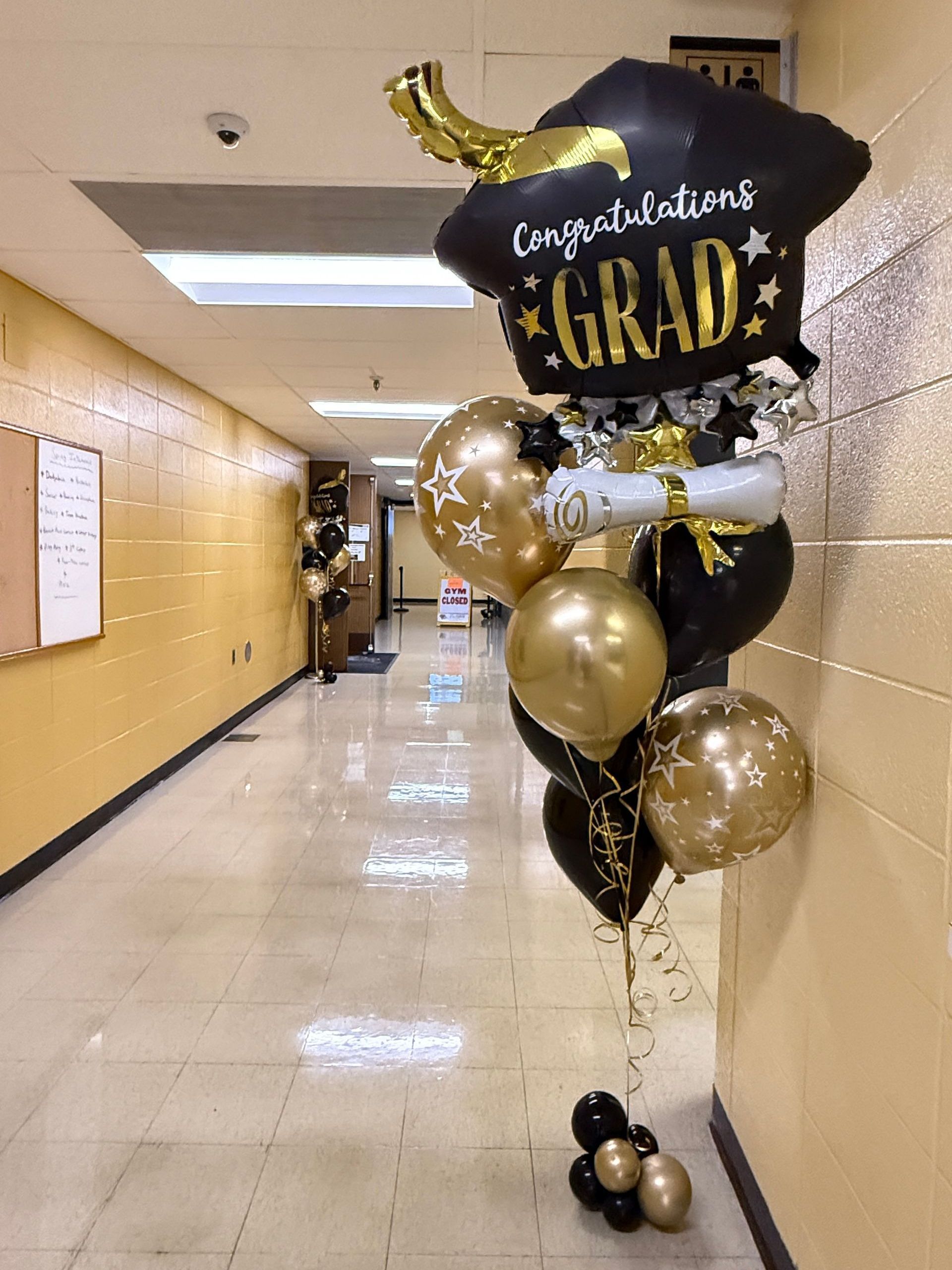 Jumbo graduation deluxe balloon bouquet, perfect for entrance decor, featuring a jumbo foil balloon, printed latex for added pizzazz, and chrome gold and black accents. A stylish grab-and-go item for any celebration.