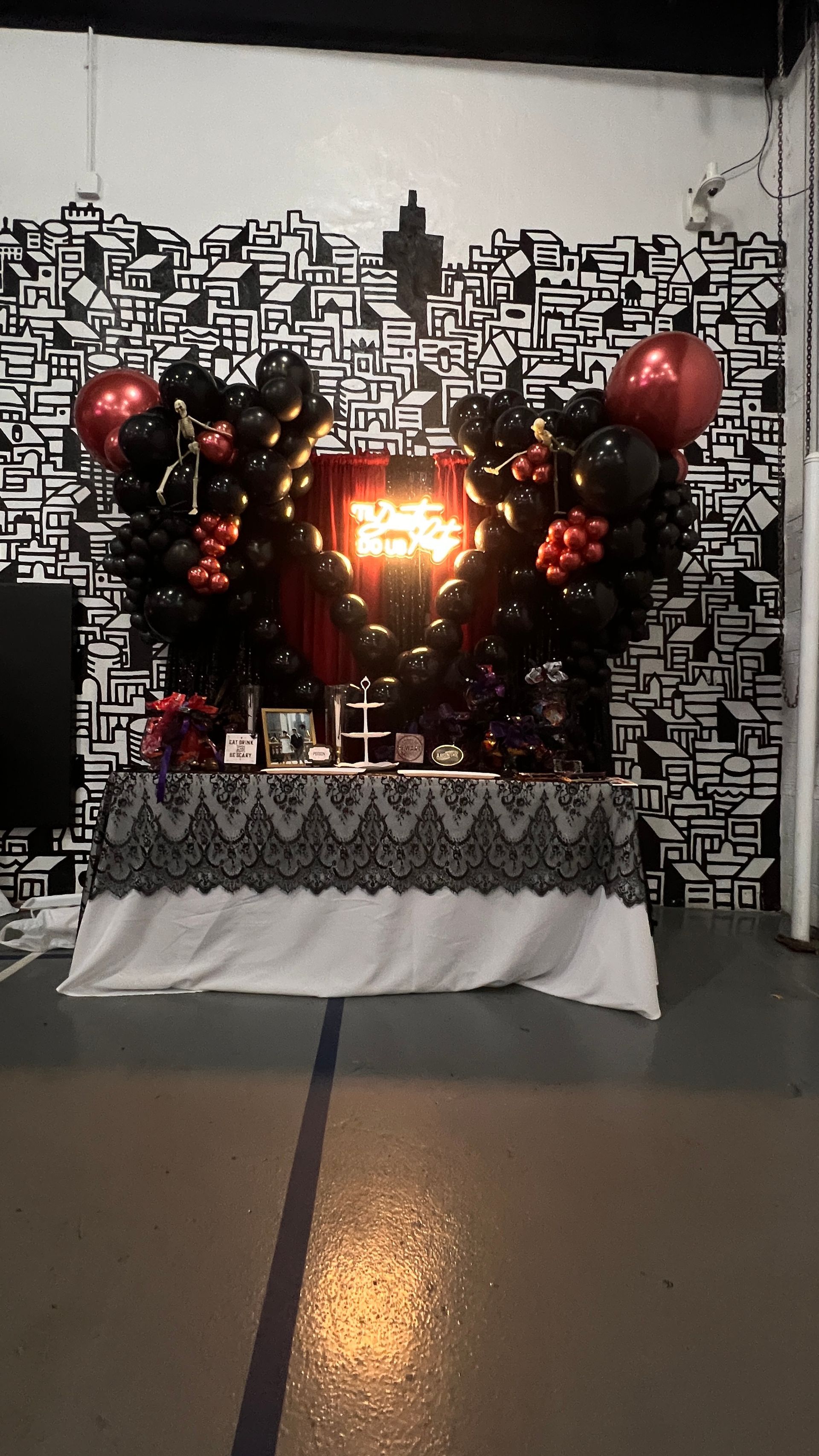 'Til Death Do Us Party' gothic-themed bridal shower in Chicago, IL, featuring an organic deluxe black balloon garland with mirror red accent balloons and skeleton decorations. Paired with black and red shimmer drapes and a stylish sweets table for a dramatic and elegant look.