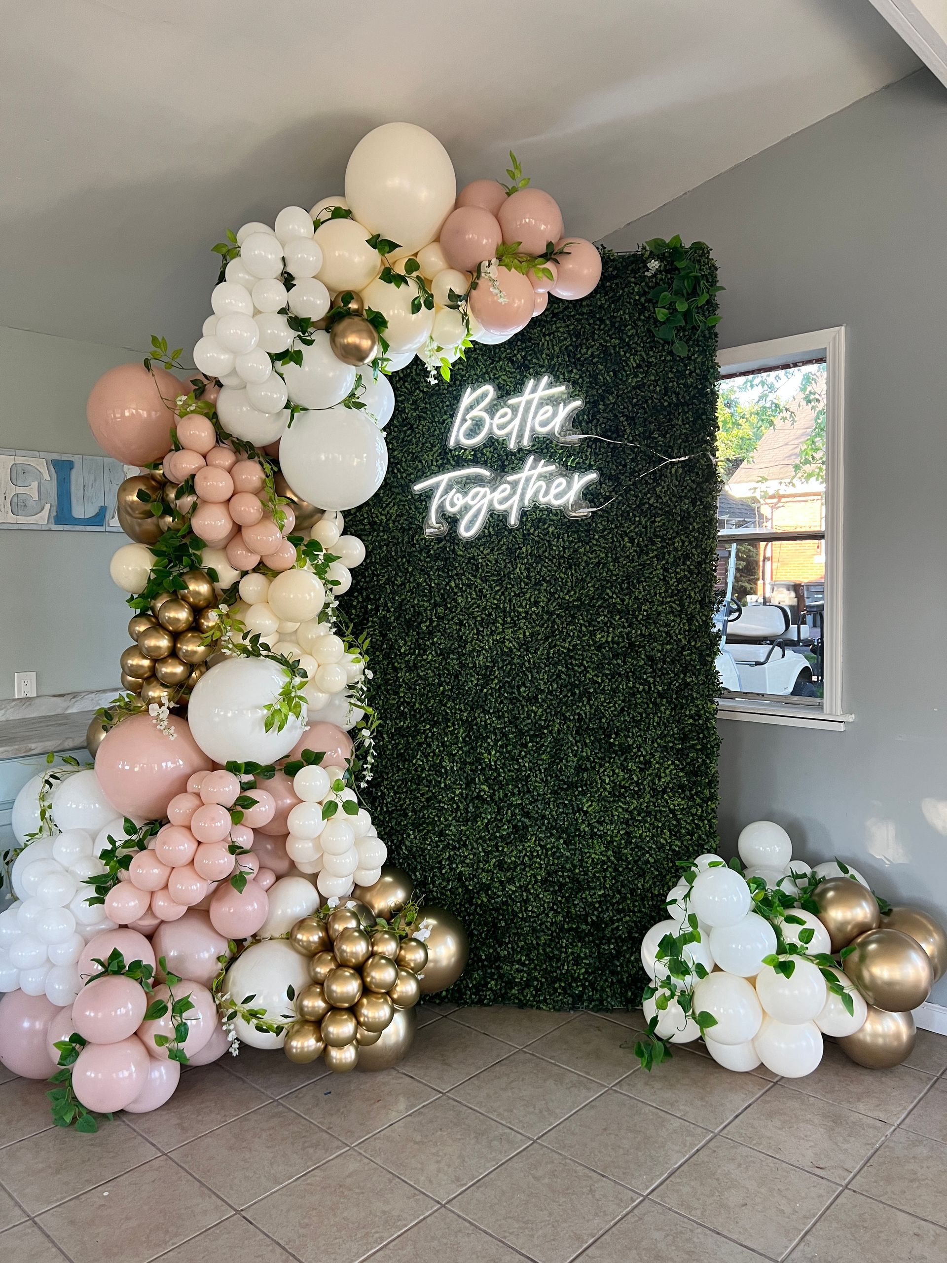 7' hedge wall with a grand luxury balloon garland in white, blush pink, and gold tones, accented with floral details. Perfect for a bridal shower, featuring an organic design and a 'Better Together' sign.
